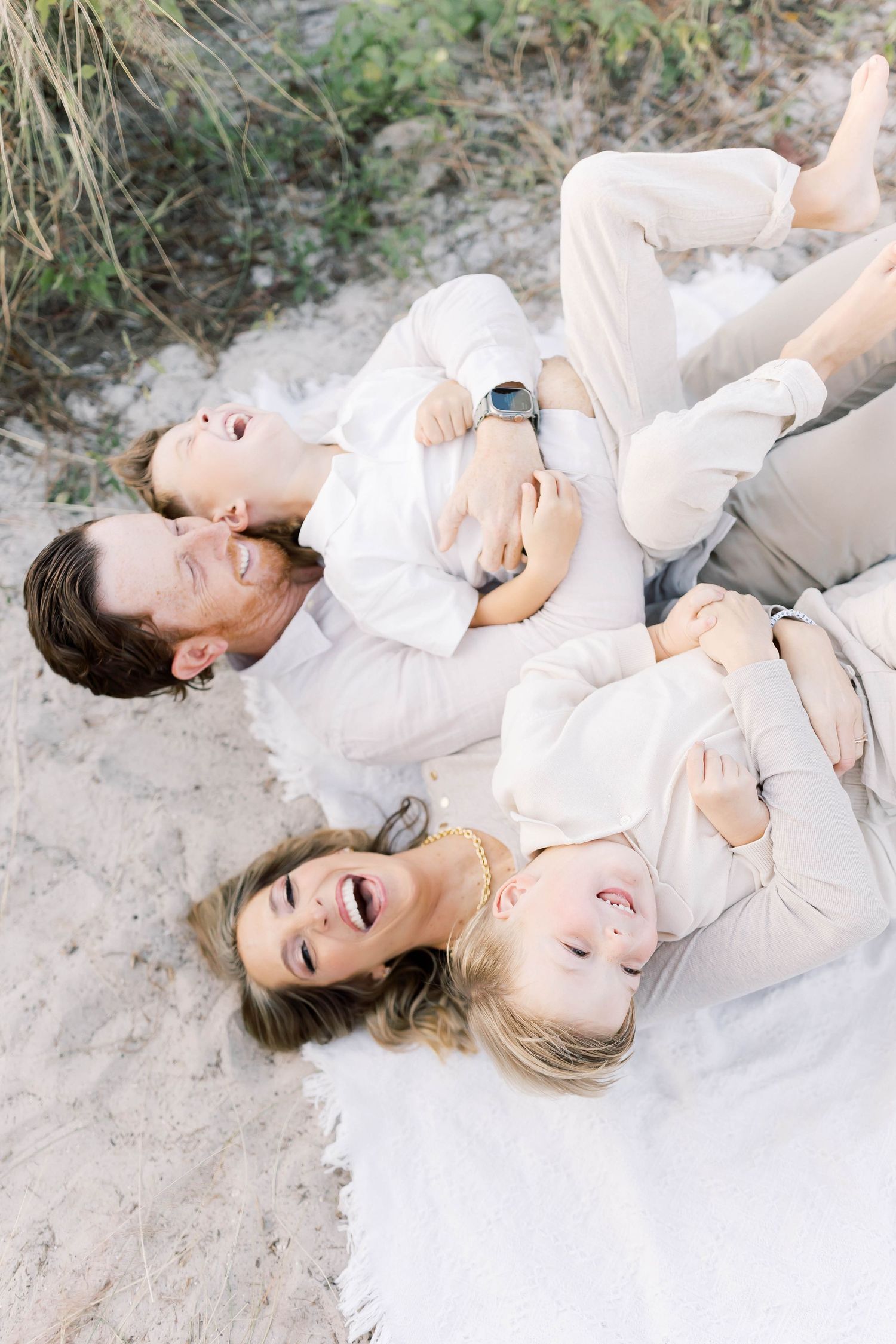Joyful family lying on sand sharing intimate laughing moments during beach photo session.