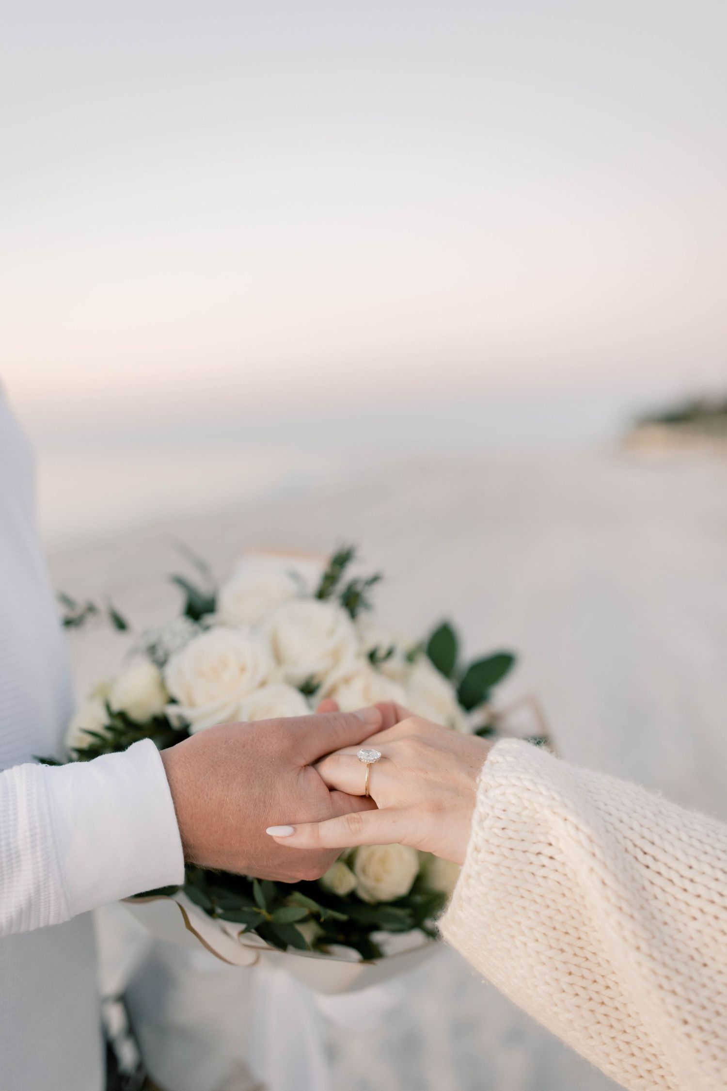 Close-up of hands exchanging white floral bouquet on beach.