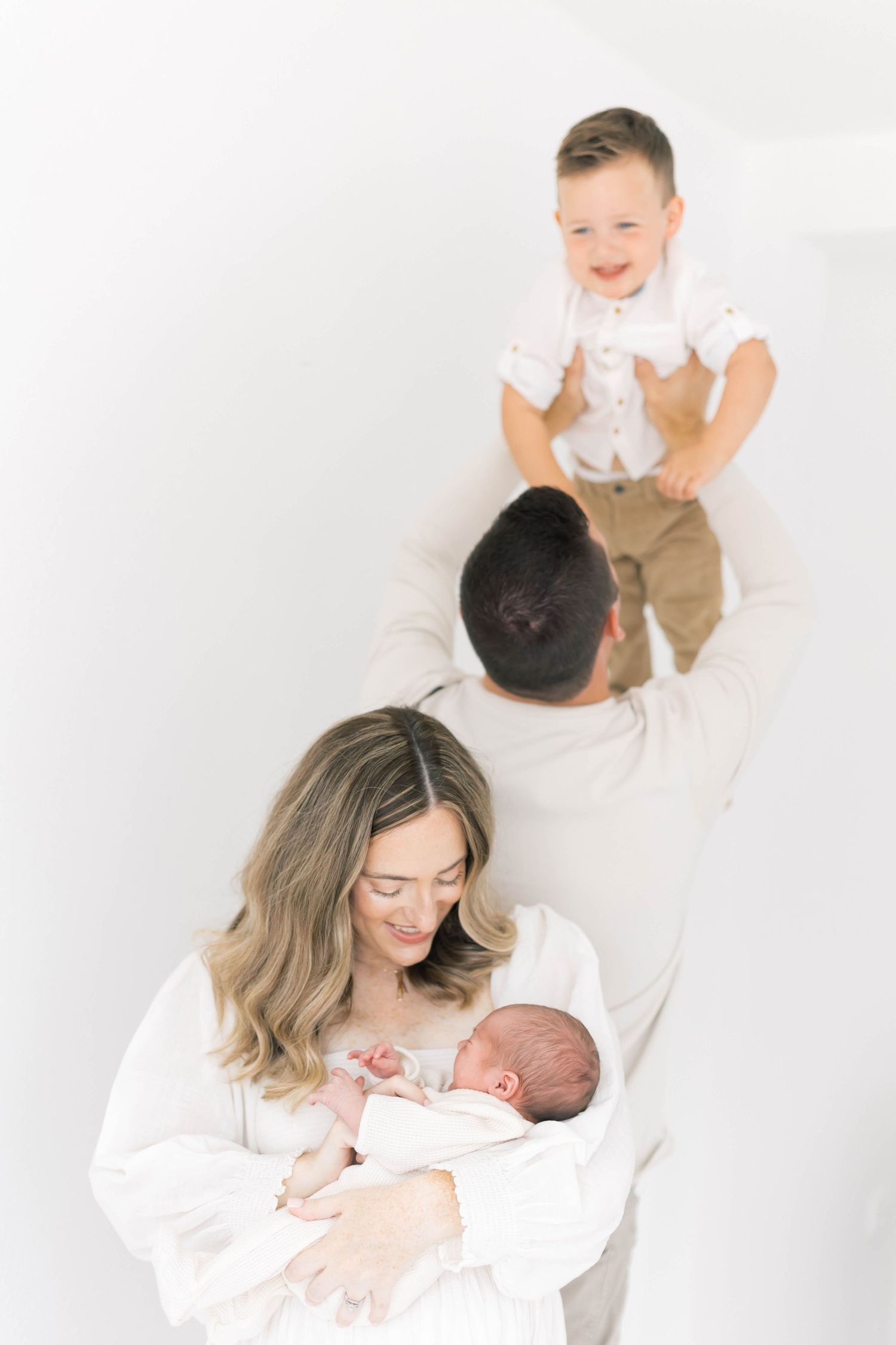 Loving family moments with newborn and toddler captured in bright white studio.
