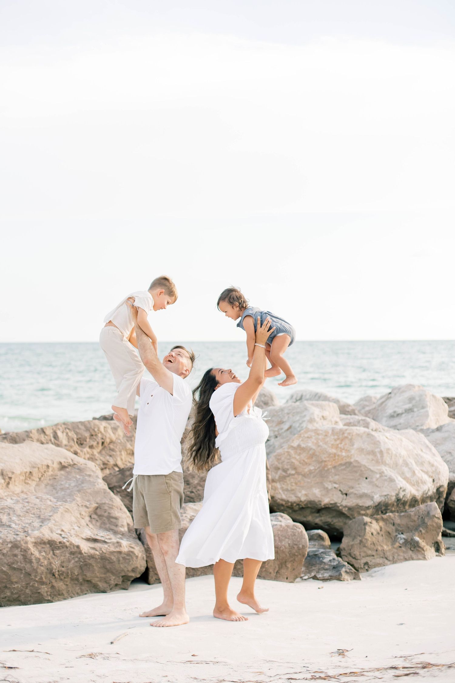 Family enjoying playful interactions on a bright sandy beach with ocean view.