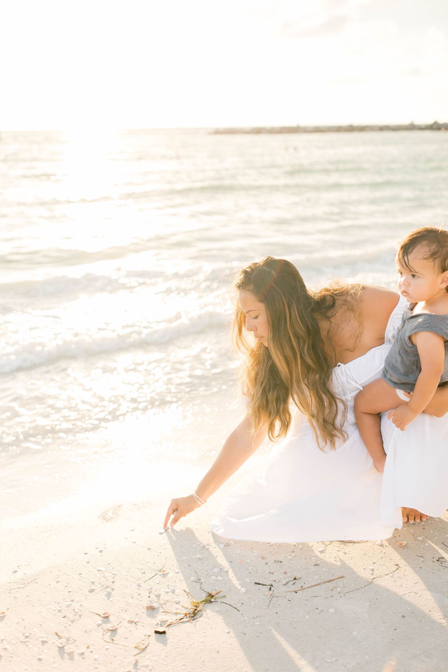 Family members bending down to explore something interesting in the sand at sunset.