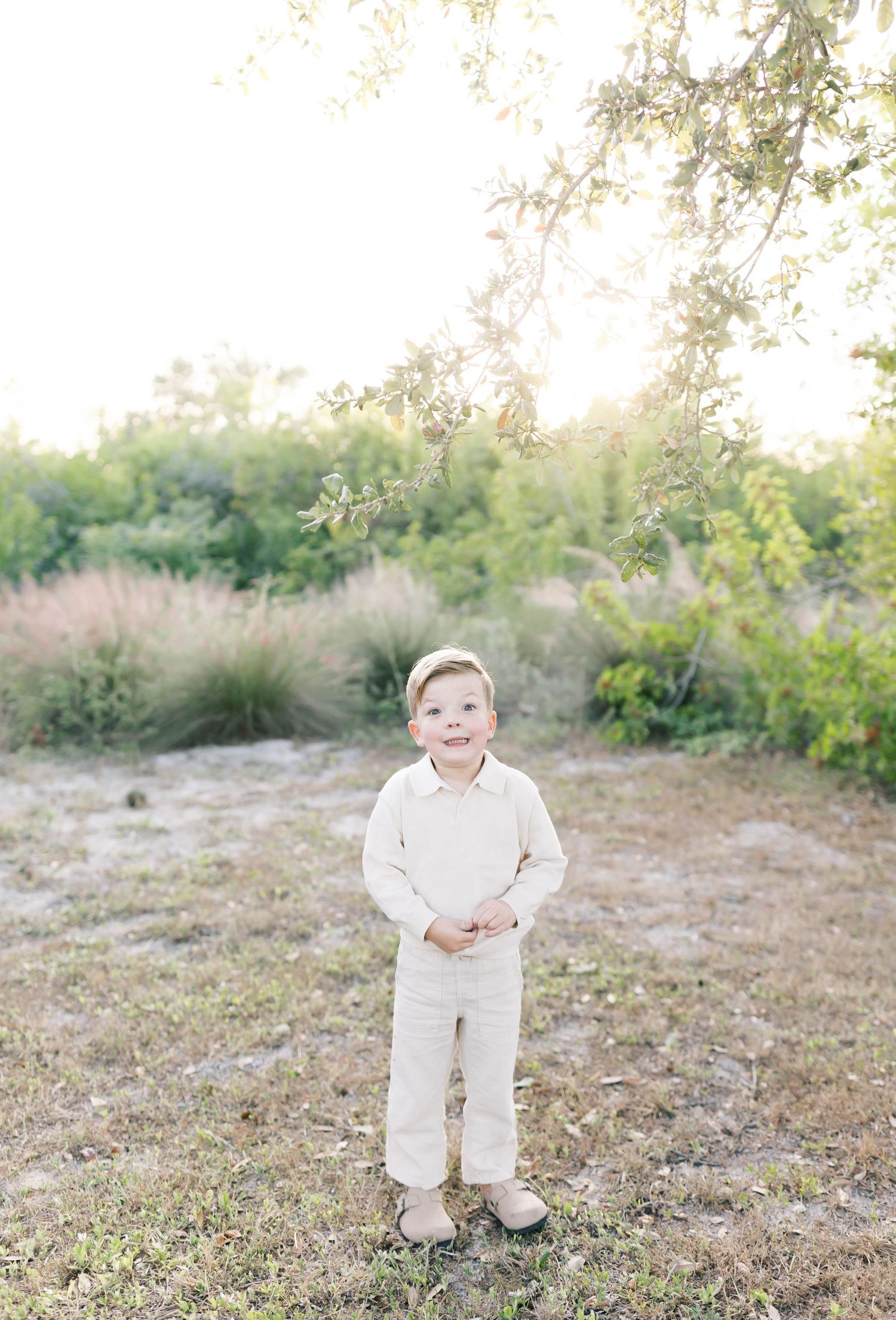 Young person in all-white attire stands alone in a natural outdoor setting with soft lighting.