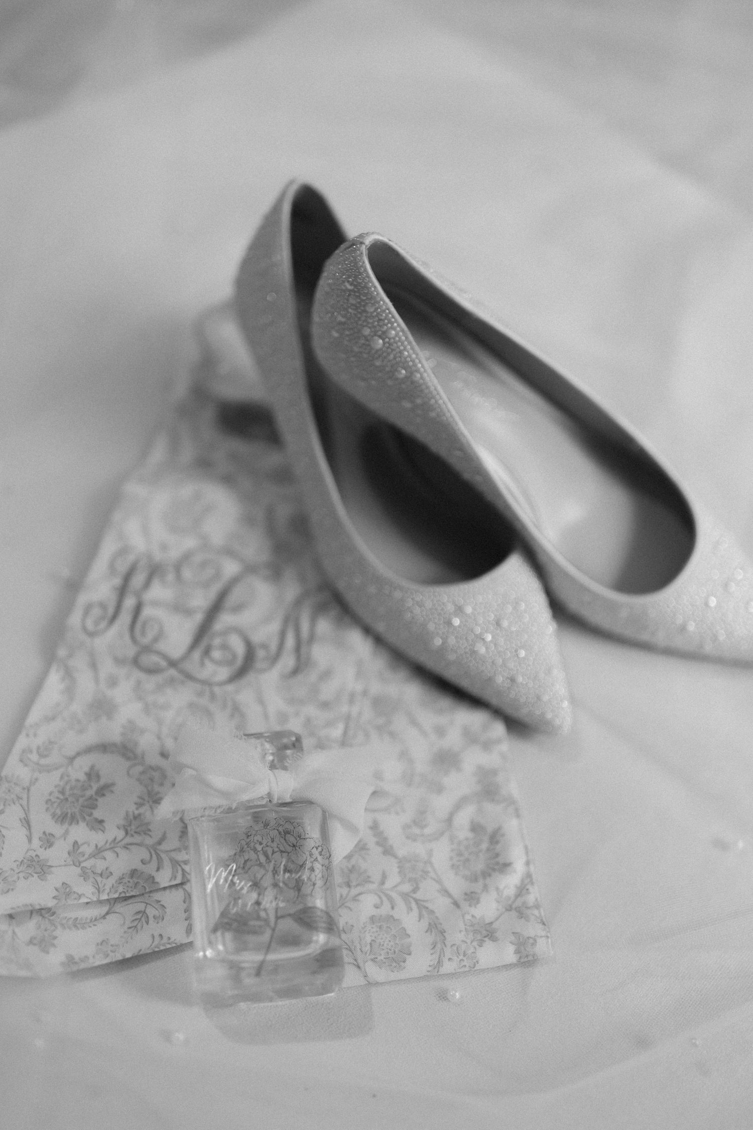 Elegant white bridal shoes placed on delicate lace fabric with intricate floral patterns.