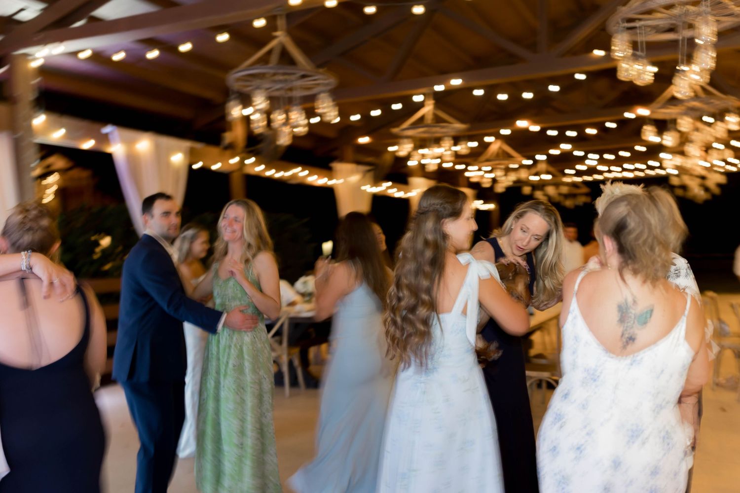 Blurred motion of wedding guests dancing under twinkling lights at reception.