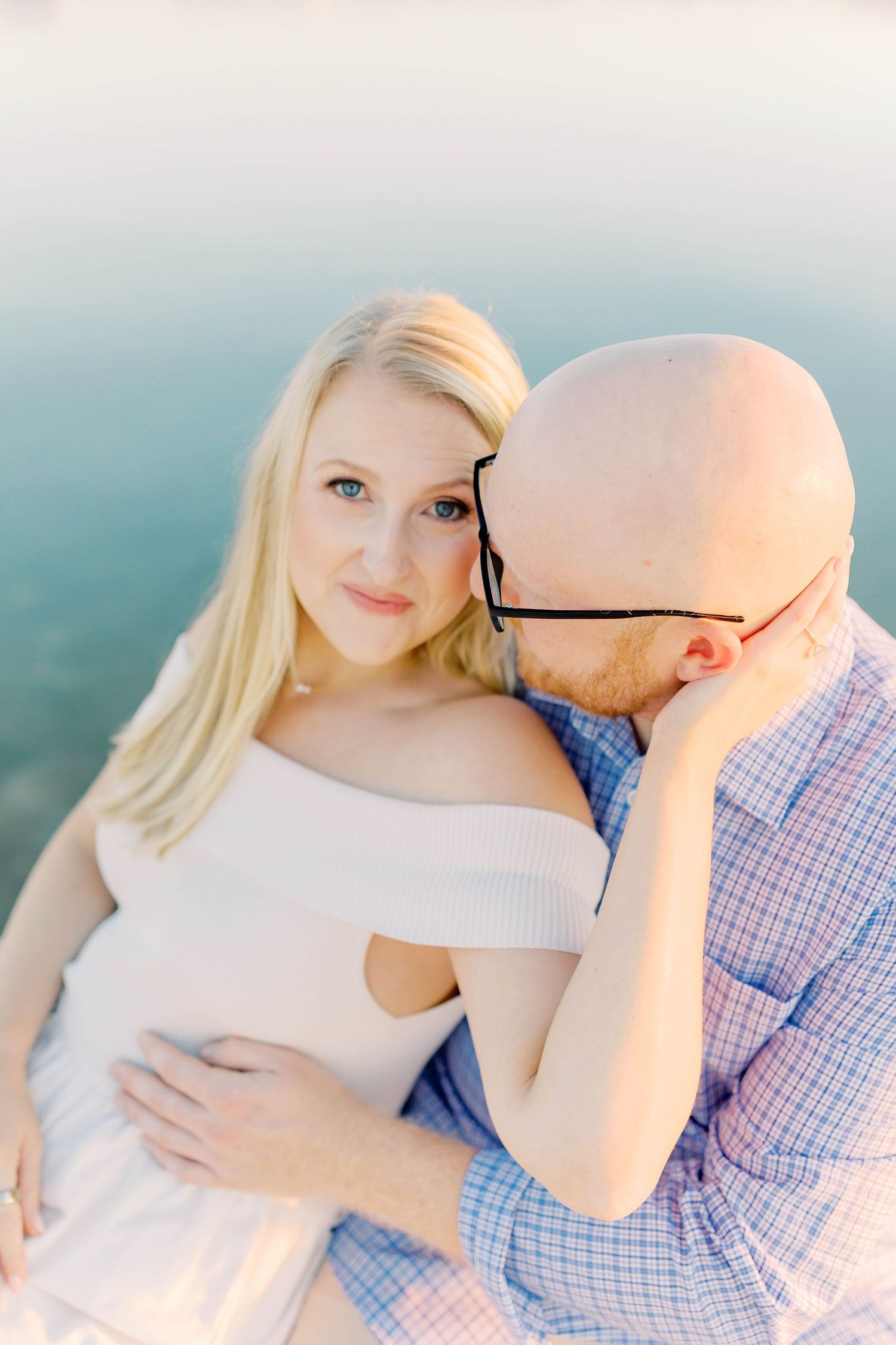 Tender embraces between couple wearing white dress and blue plaid shirt in dreamy lighting.