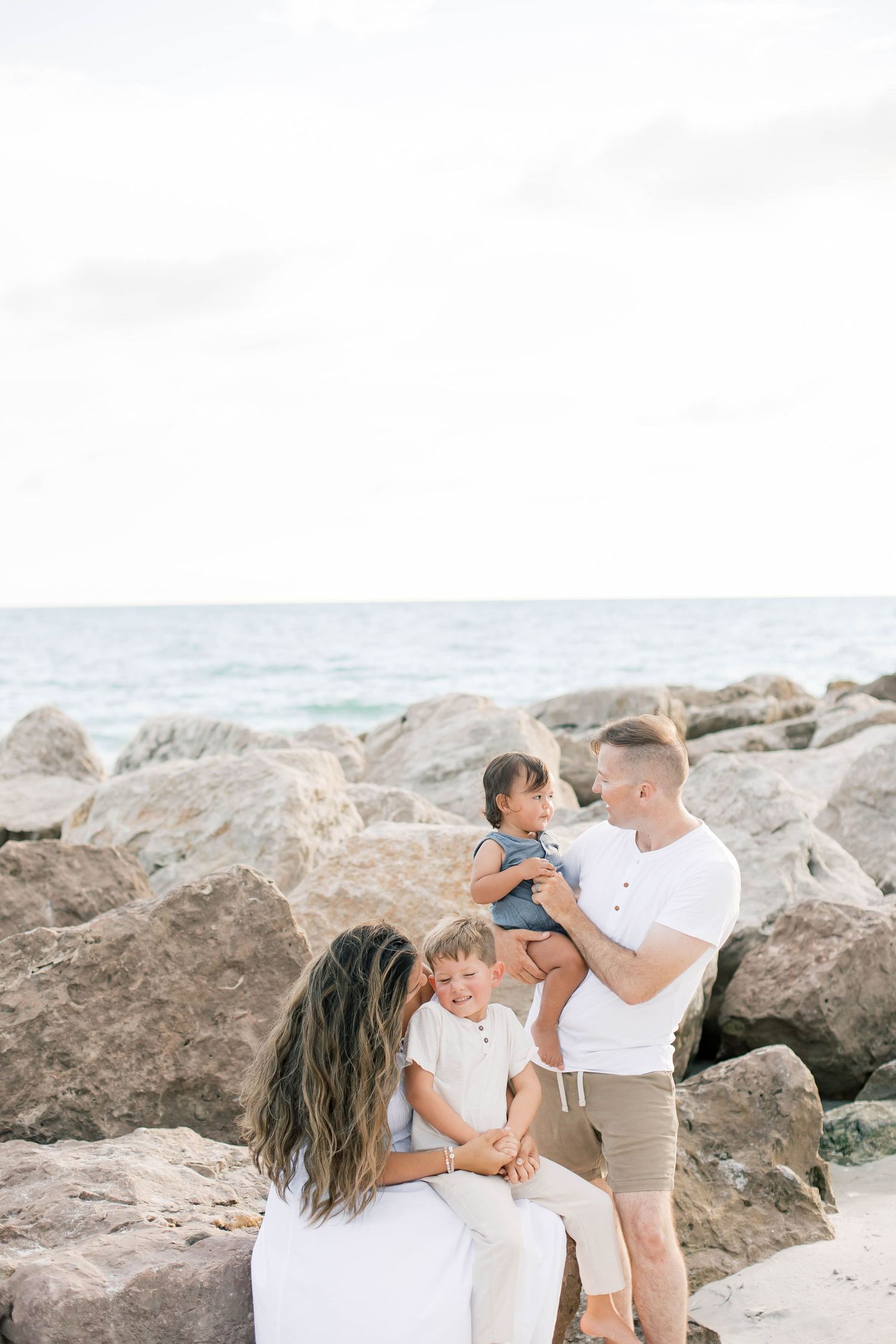 A family shares joyful moments together on a beach with large rocks and ocean views.