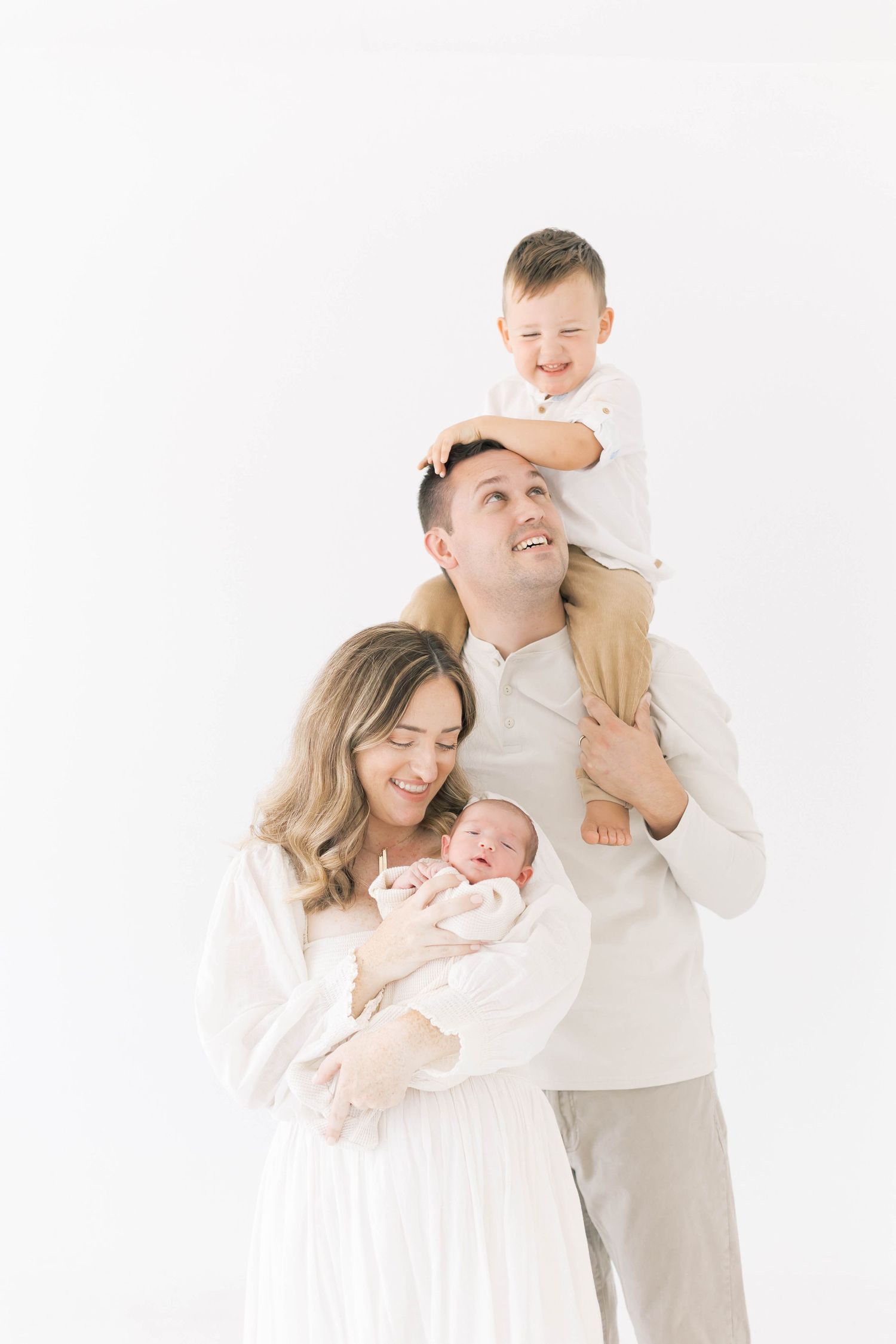 A joyful family moment captured in soft white tones against a minimalist backdrop.