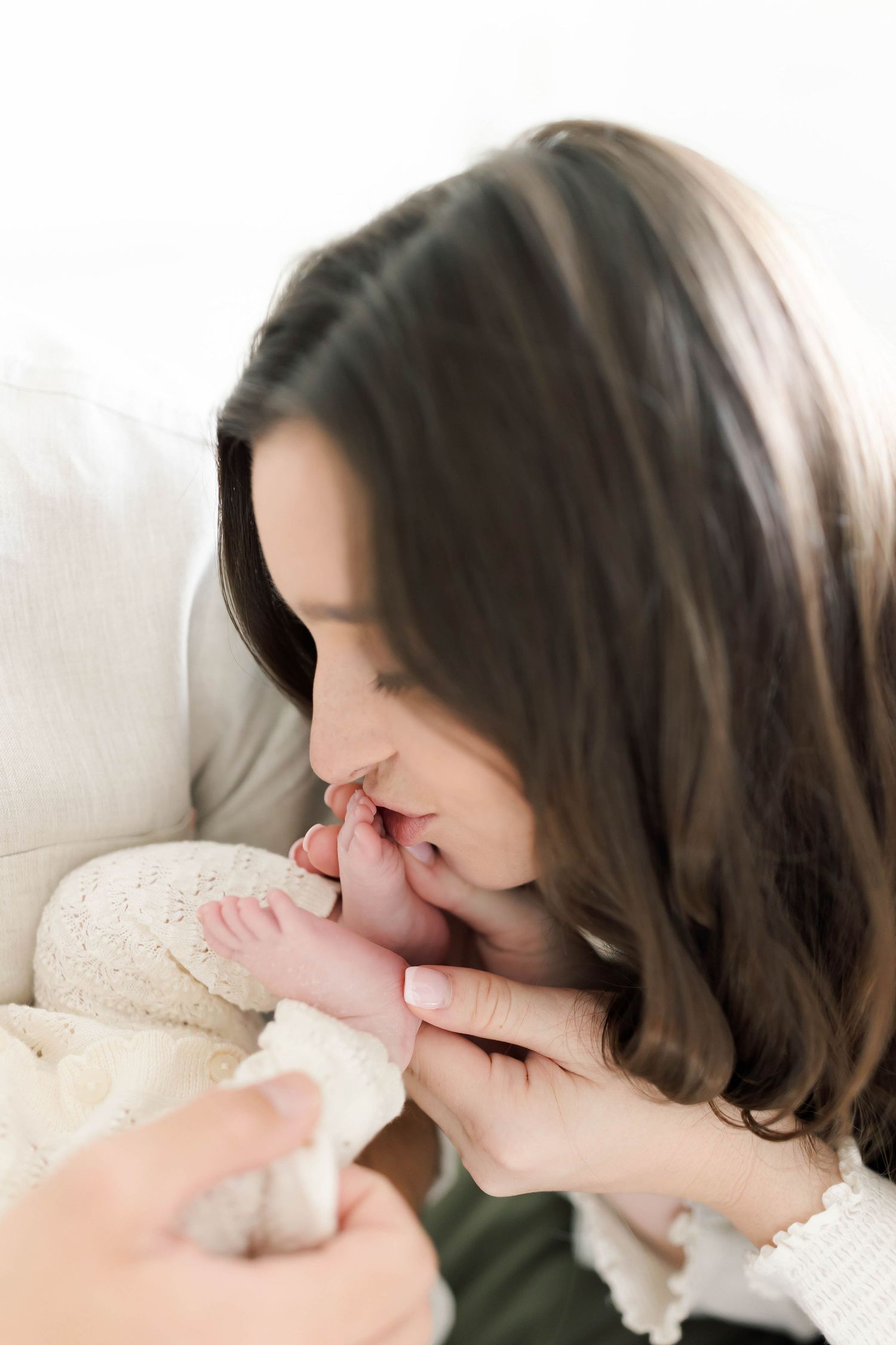 Tender moment as parent kisses newborn's tiny feet wrapped in white blanket.