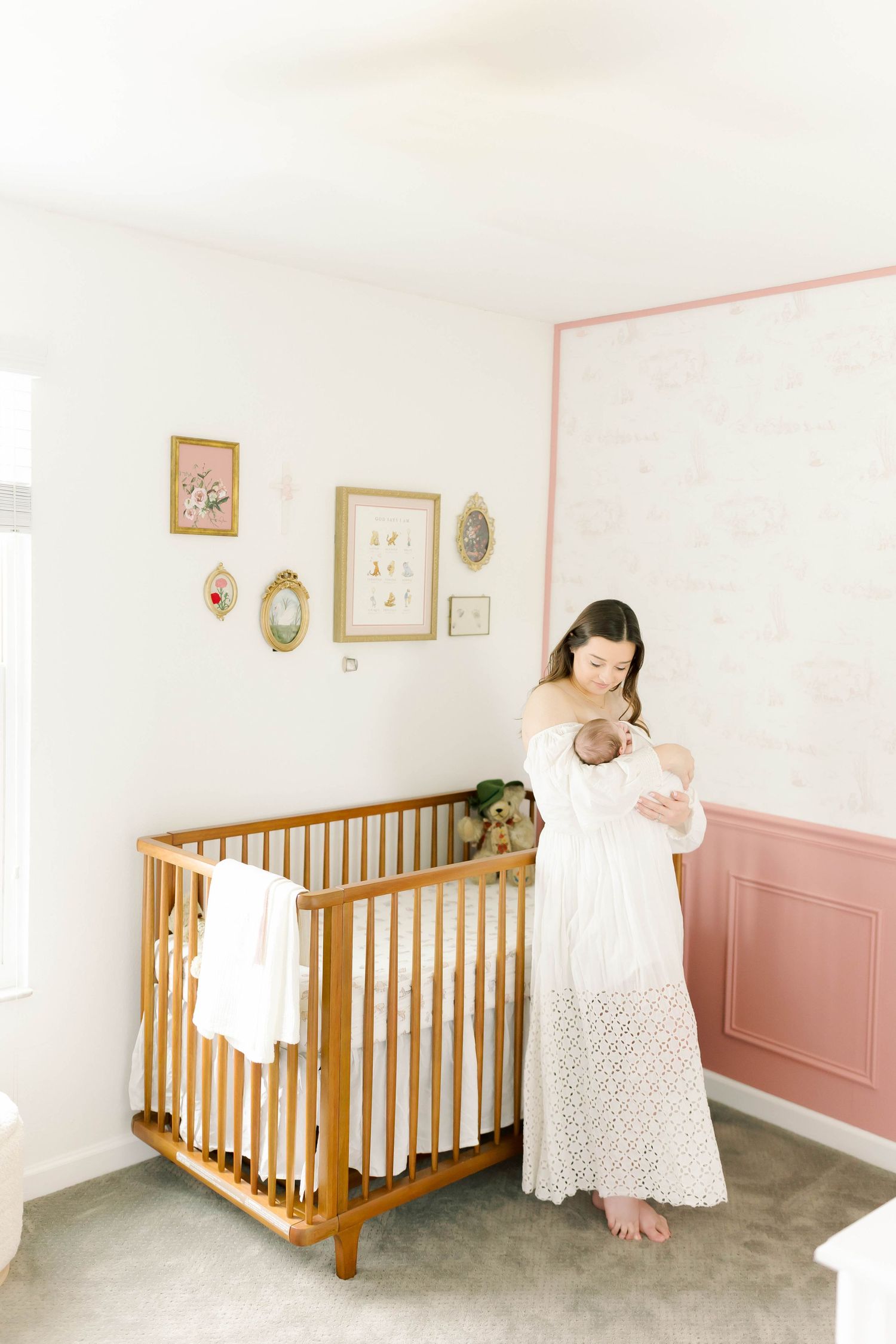 A nursery room with wooden crib, pink wainscoting, and wall art featuring someone holding a baby.