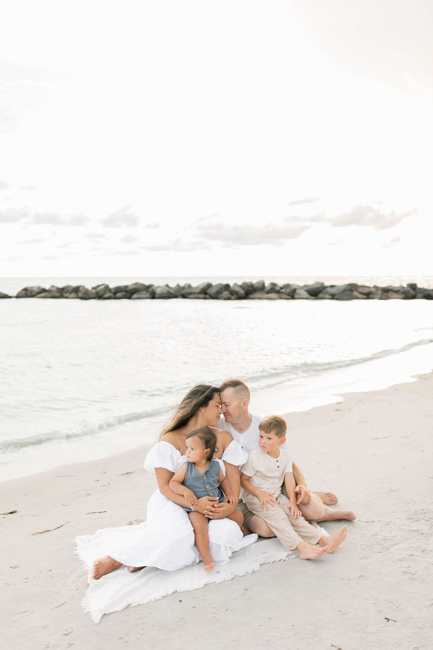 Family photo session on a serene beach with rocky coastline in the background.