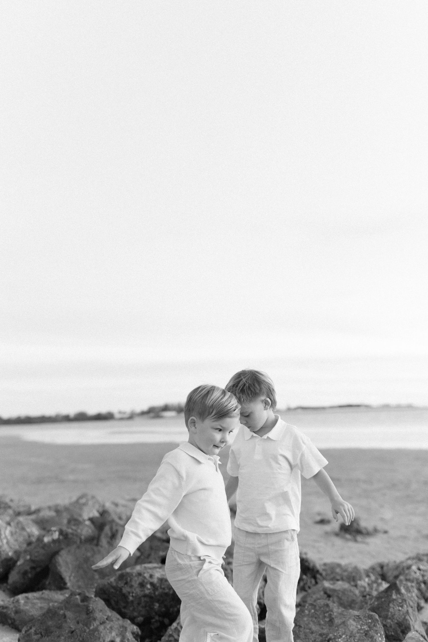 Children play among coastal rocks during black and white beach photoshoot.