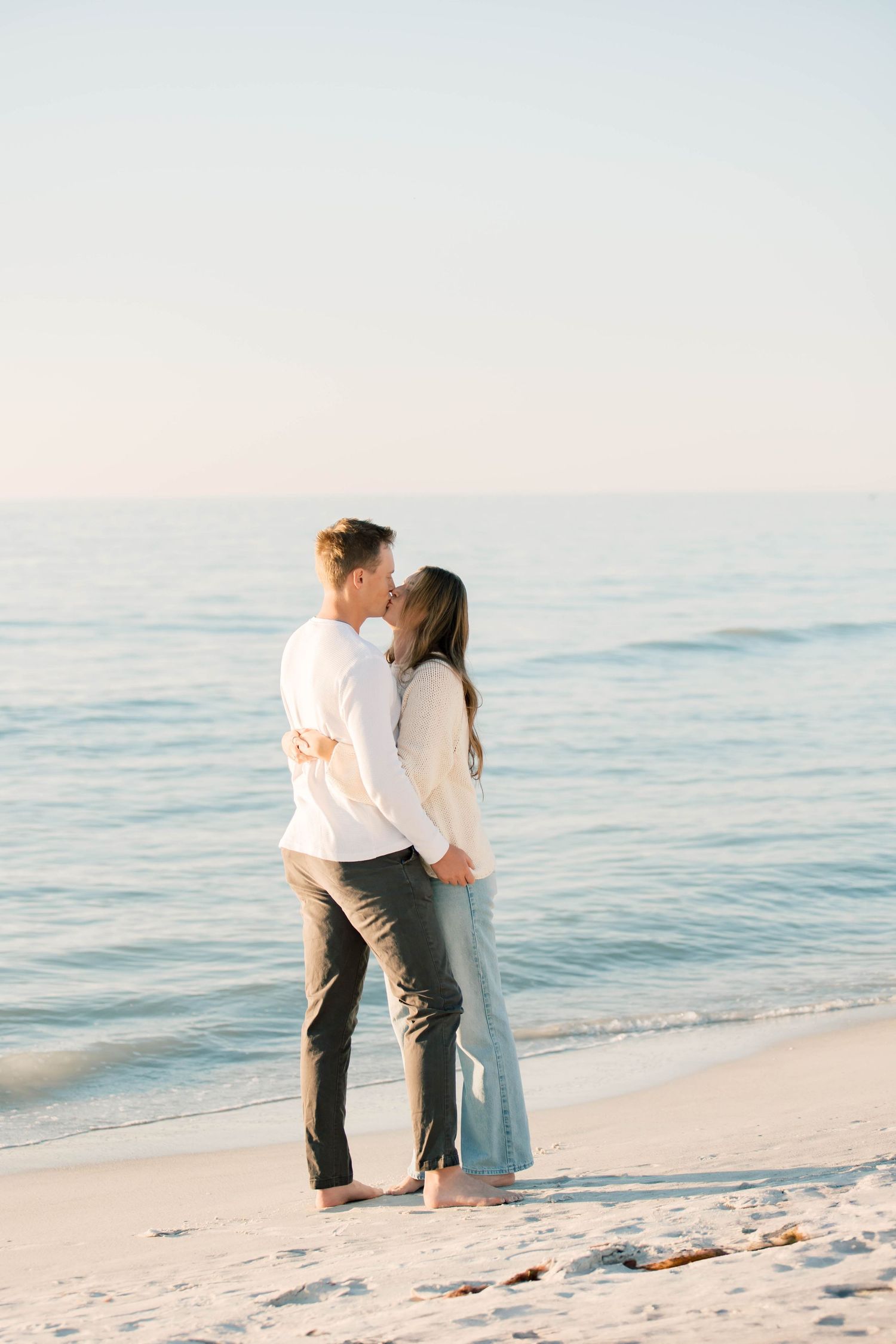 Two people embrace on a sunny beach with gentle waves and white sand creating a romantic scene.