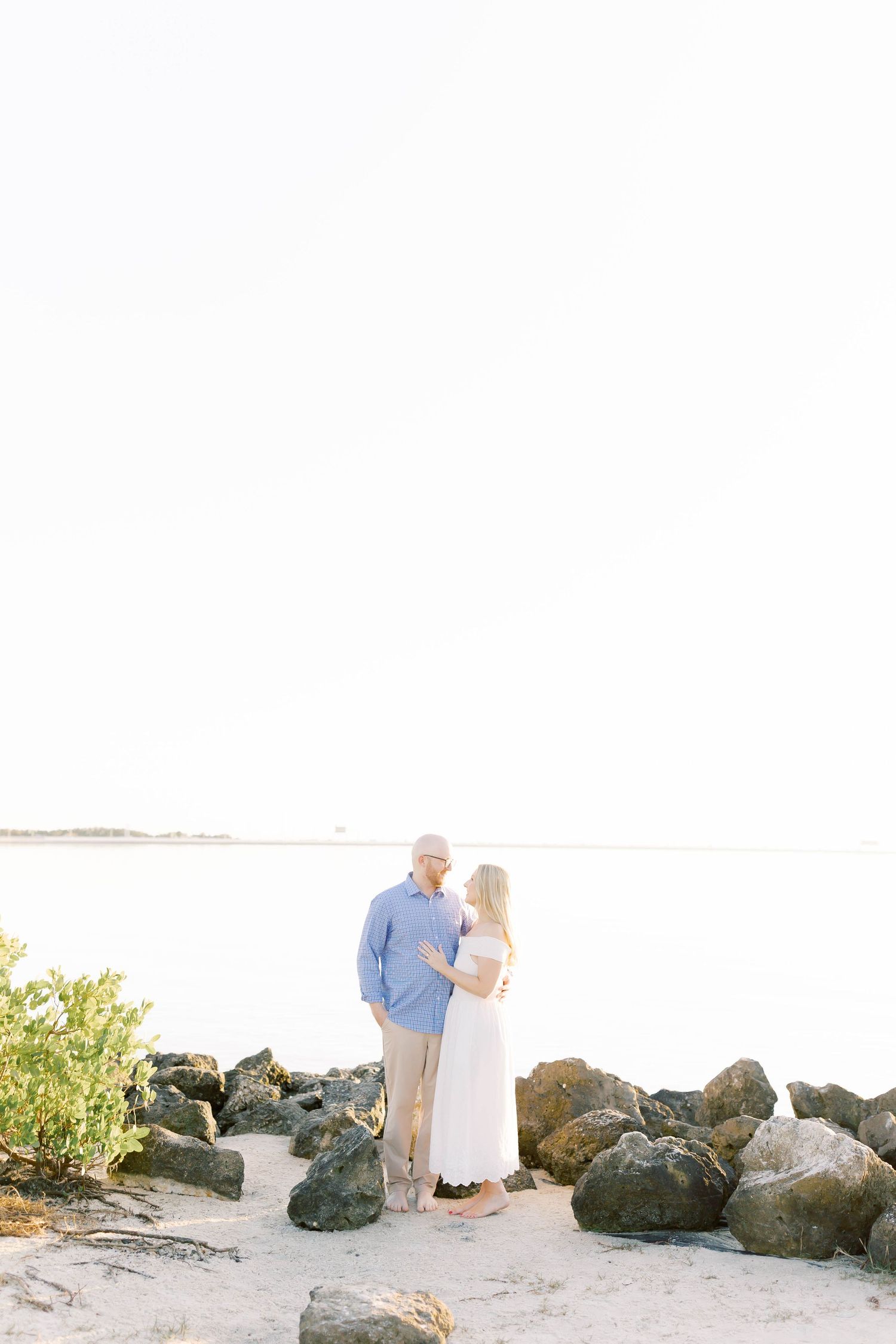Couple poses near rocky outcrop on sandy beach during golden hour.