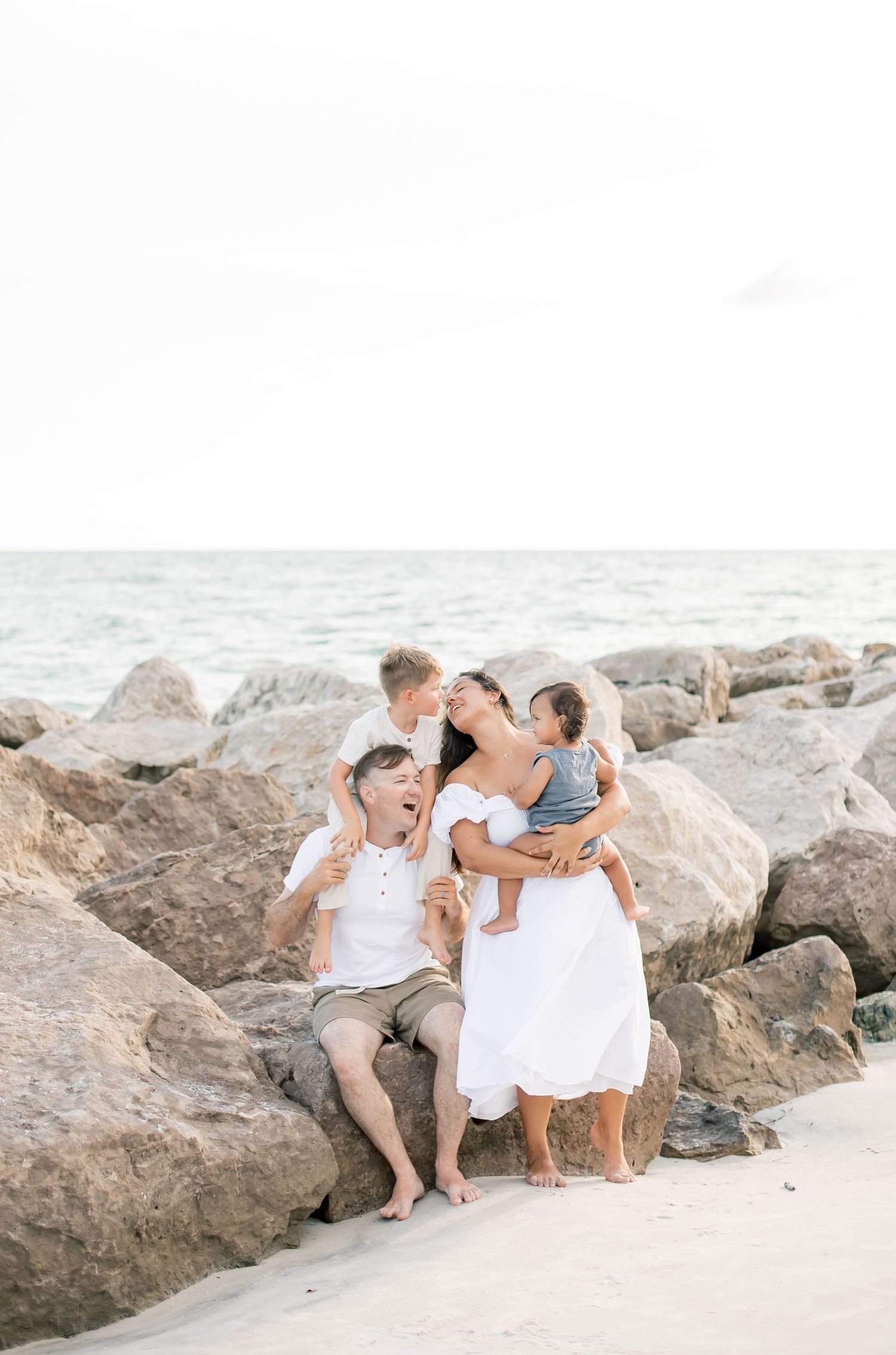 Candid family portrait showing affection while sitting on coastal rocks at the beach.