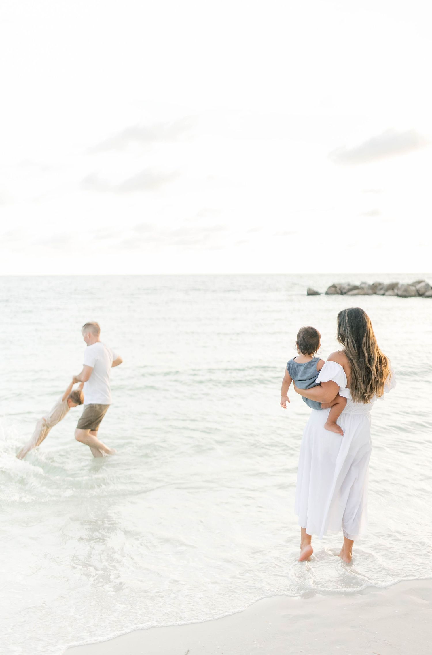 Family playing in the gentle waves during a beach photoshoot in white attire.