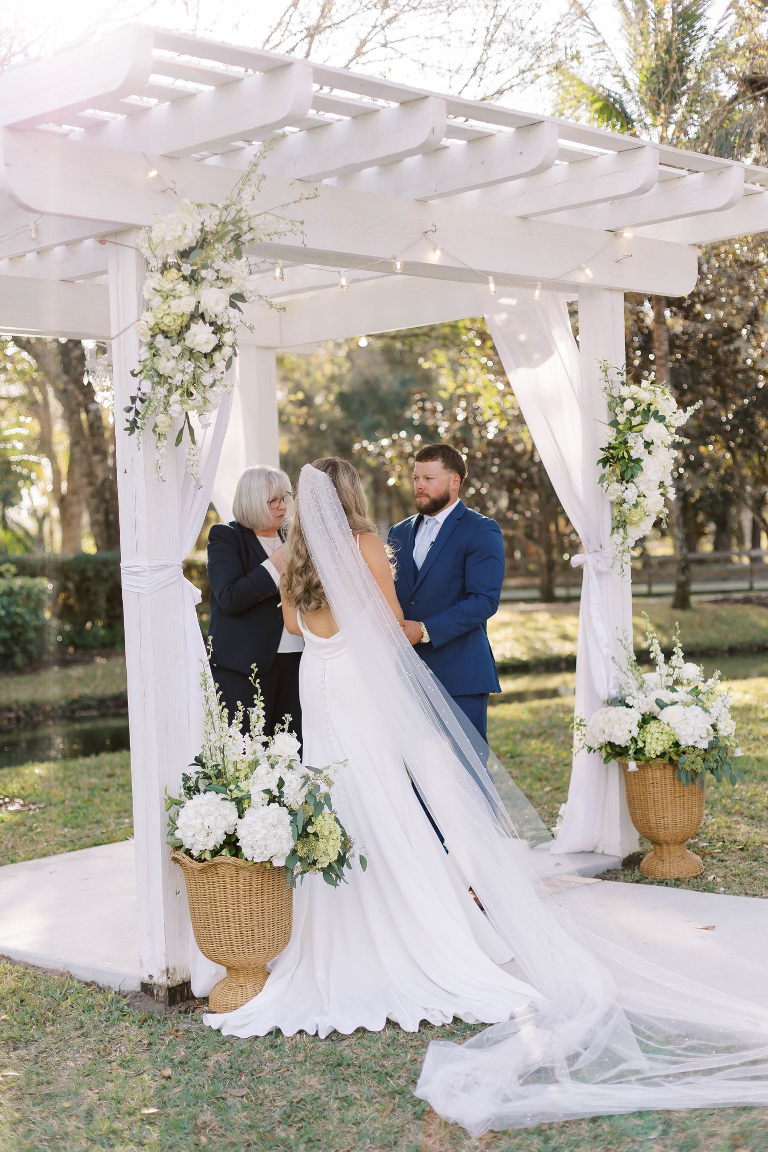 Outdoor wedding ceremony setup with white pergola and floral decorations in natural setting.