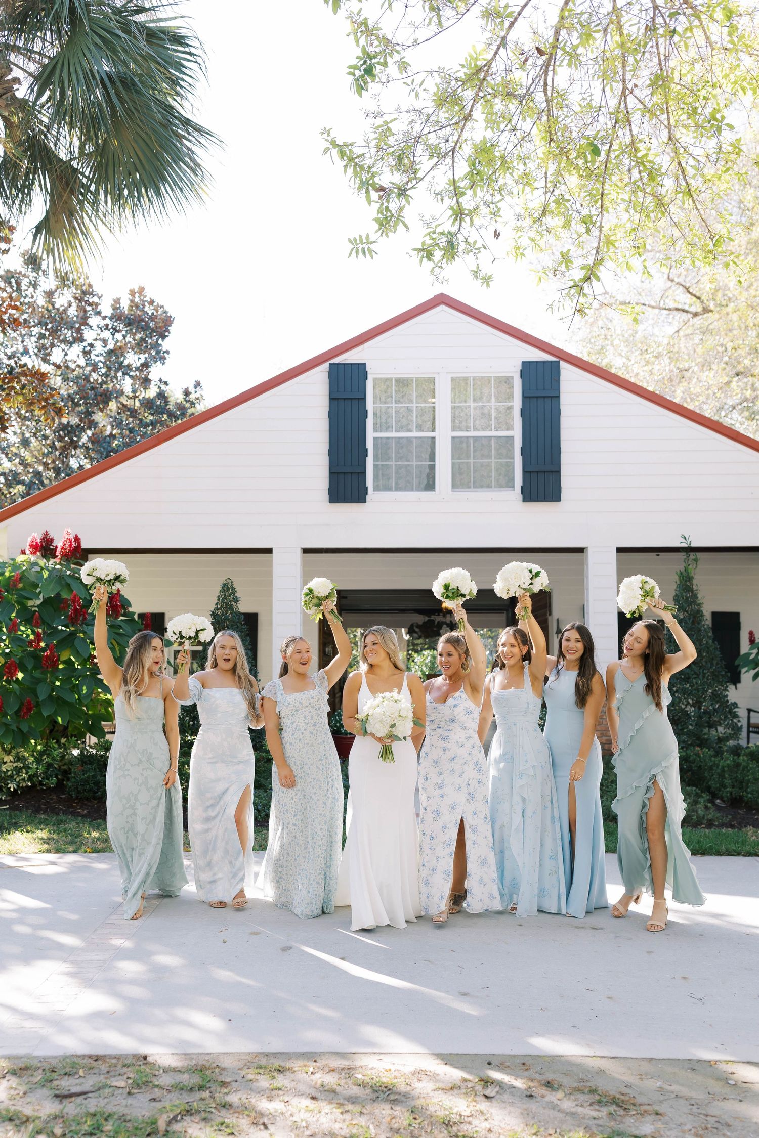 Bridesmaids in light blue dresses celebrate together outside a white wedding venue.