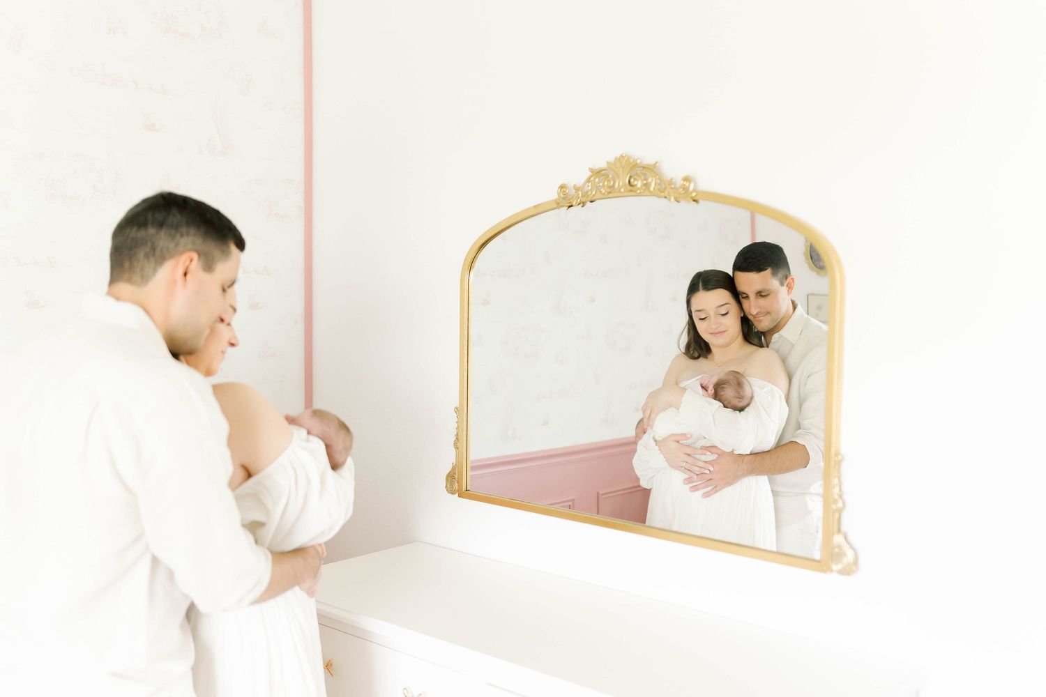A couple with their newborn baby captured in reflection of an ornate gold mirror.
