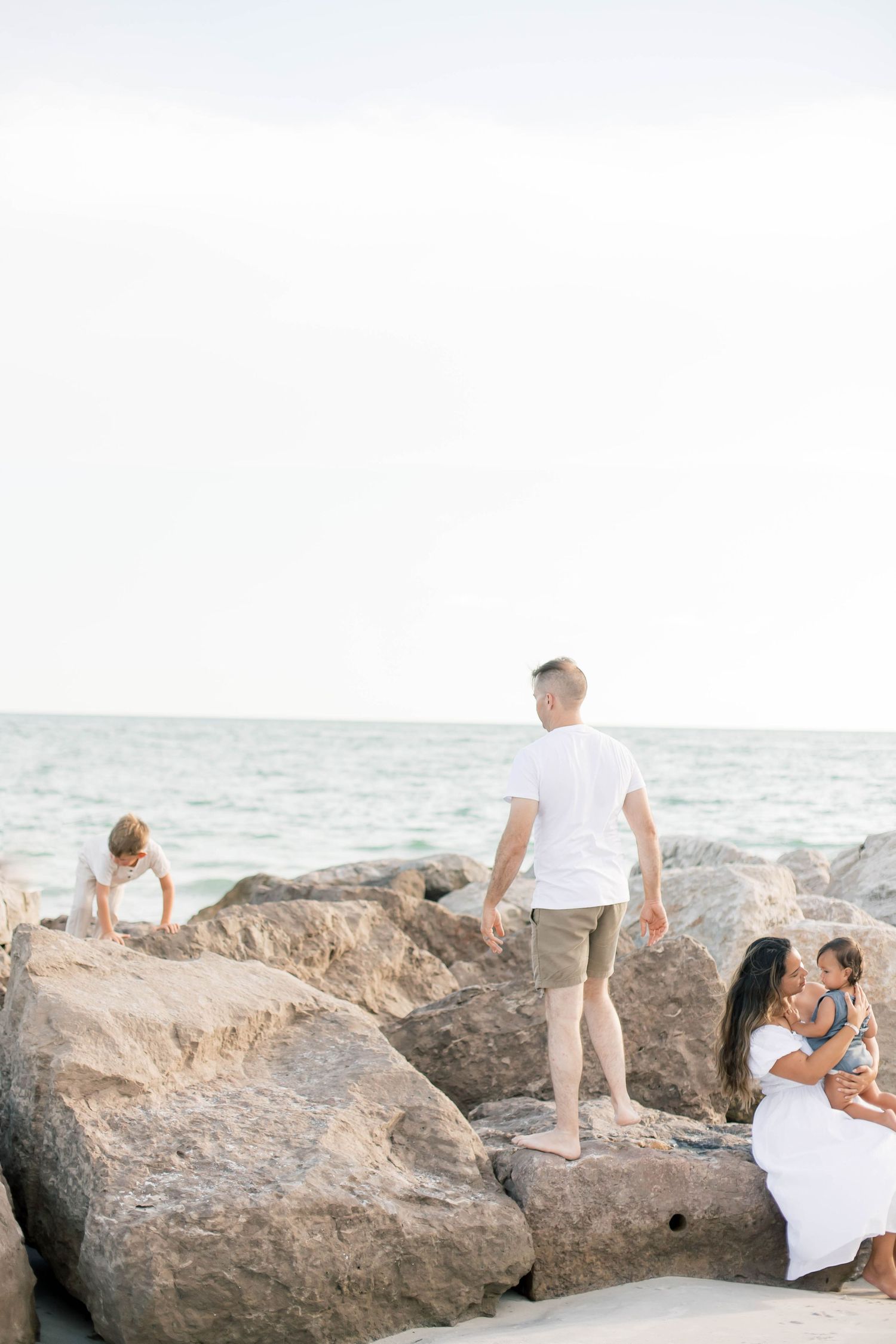 Family photoshoot on a scenic beach with large coastal rocks.