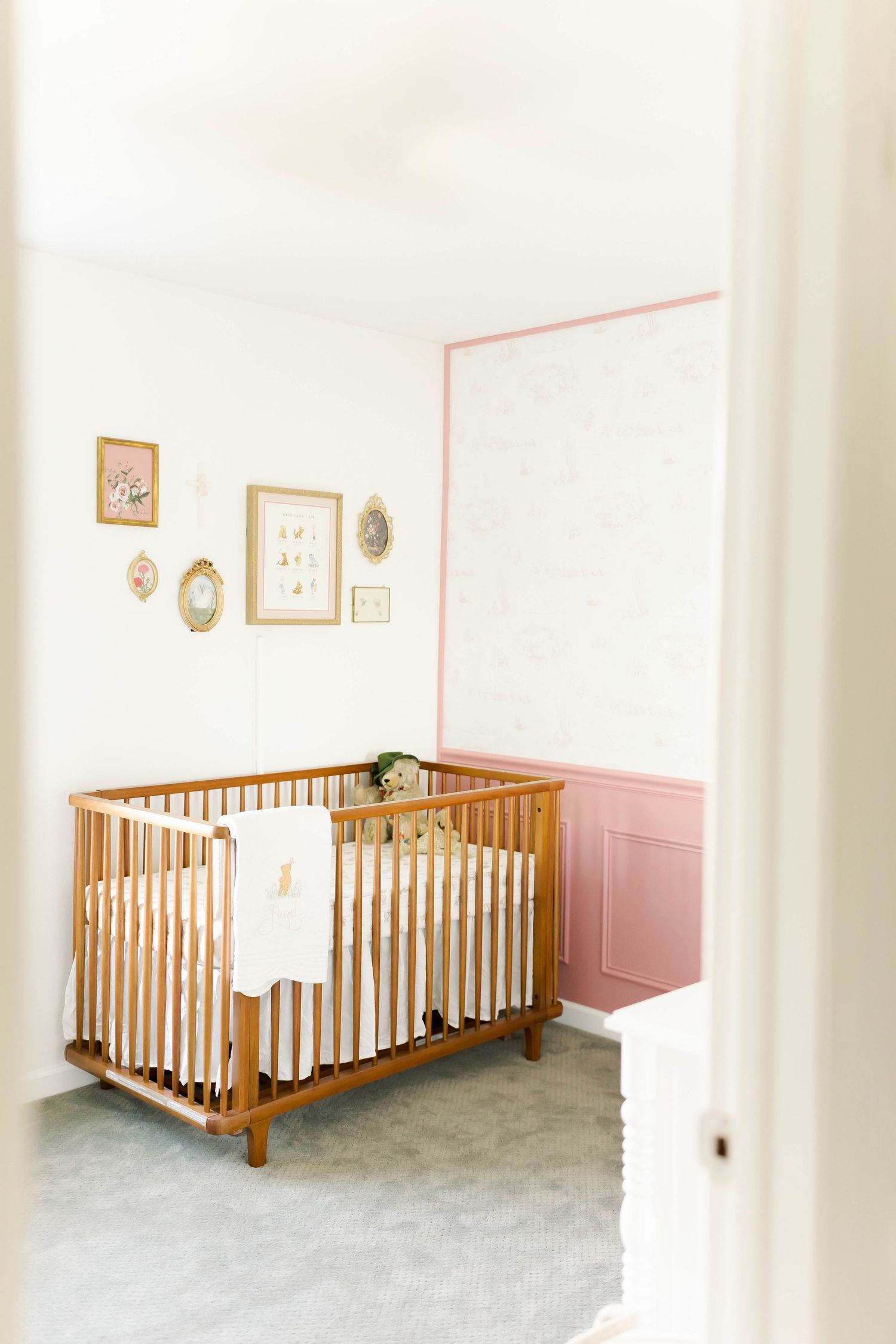 Wooden crib with spindle rails positioned against pink and white walls in nursery.