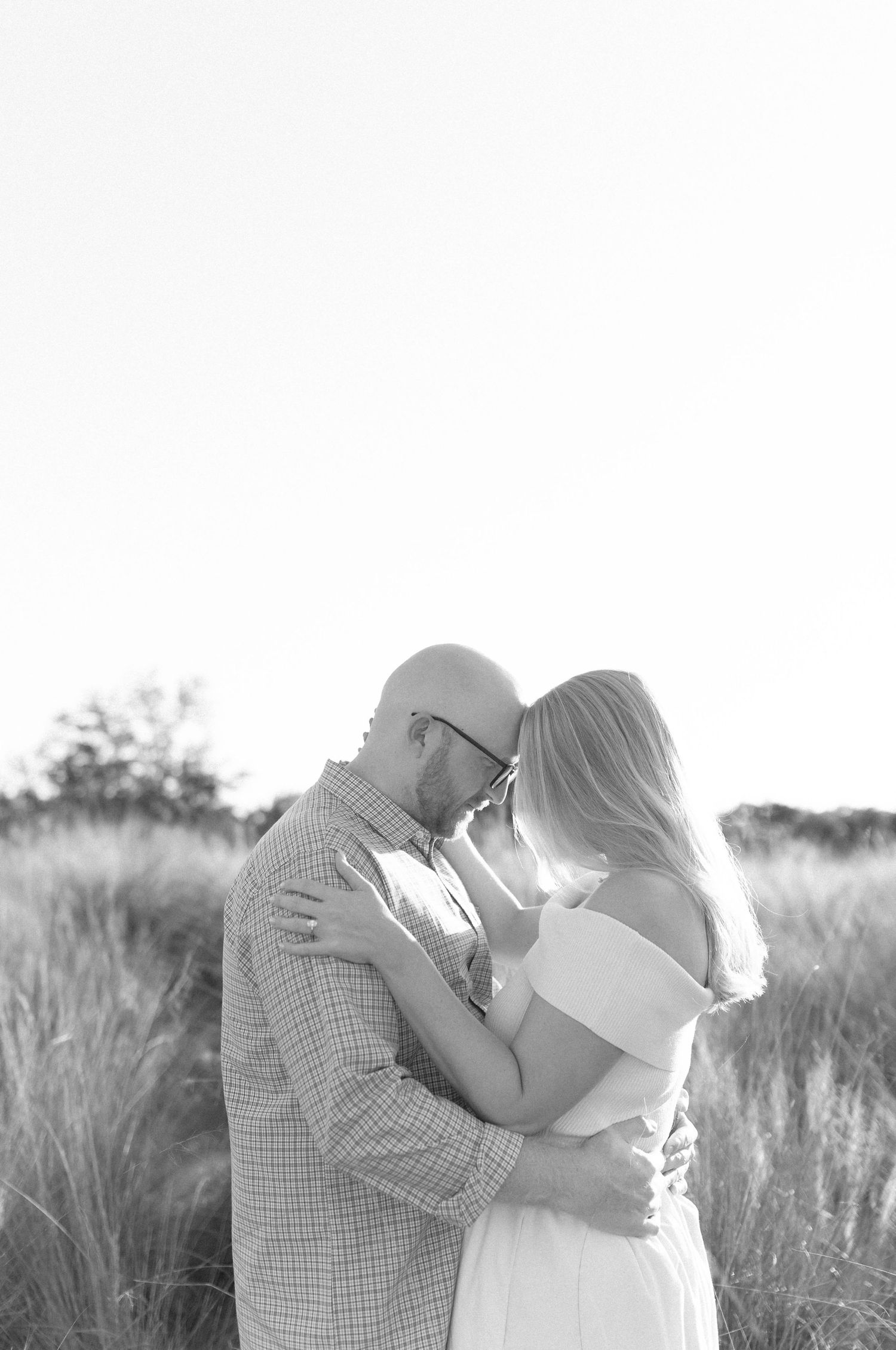 Black and white portrait of couple sharing tender moment in field of grass.