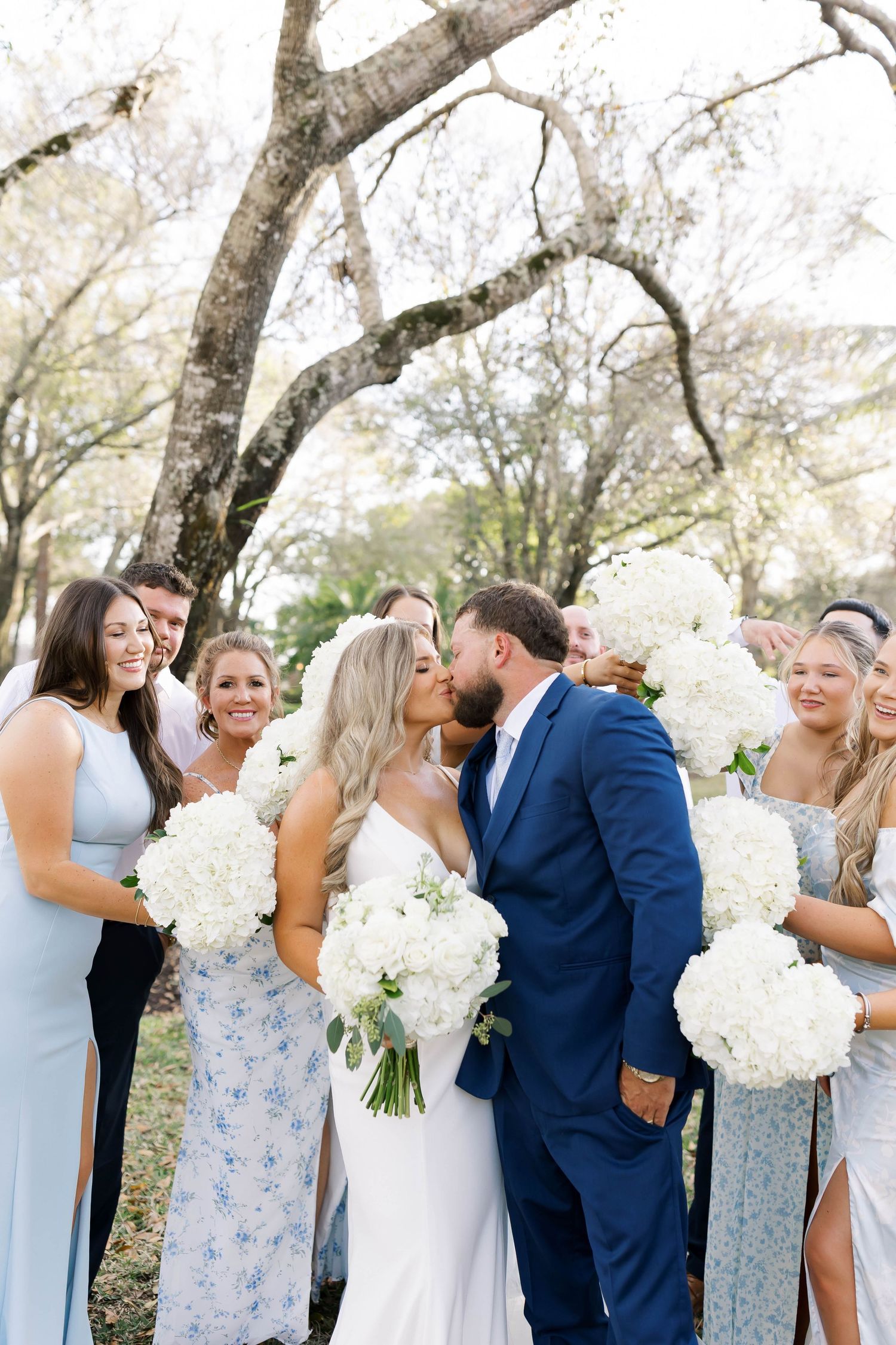 Wedding party stands in line wearing coordinated white dresses and navy suits.