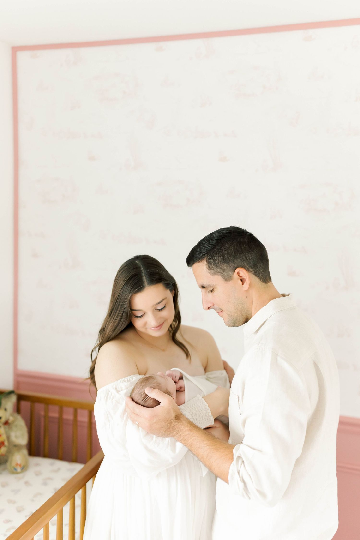 A tender nursery moment as a couple in white and beige admire their baby.