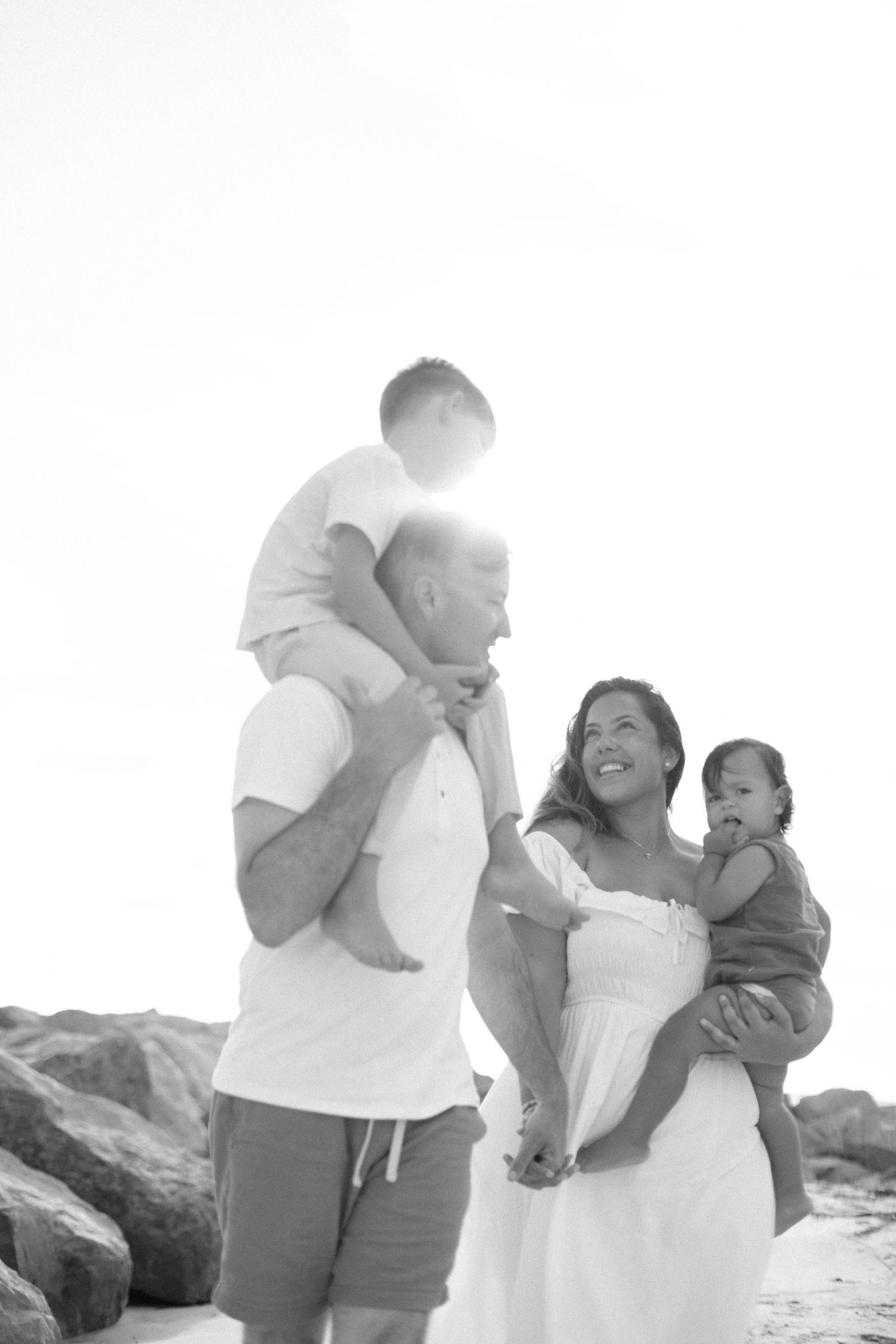 Black and white beach photos showing tender family moments against a rocky shoreline.