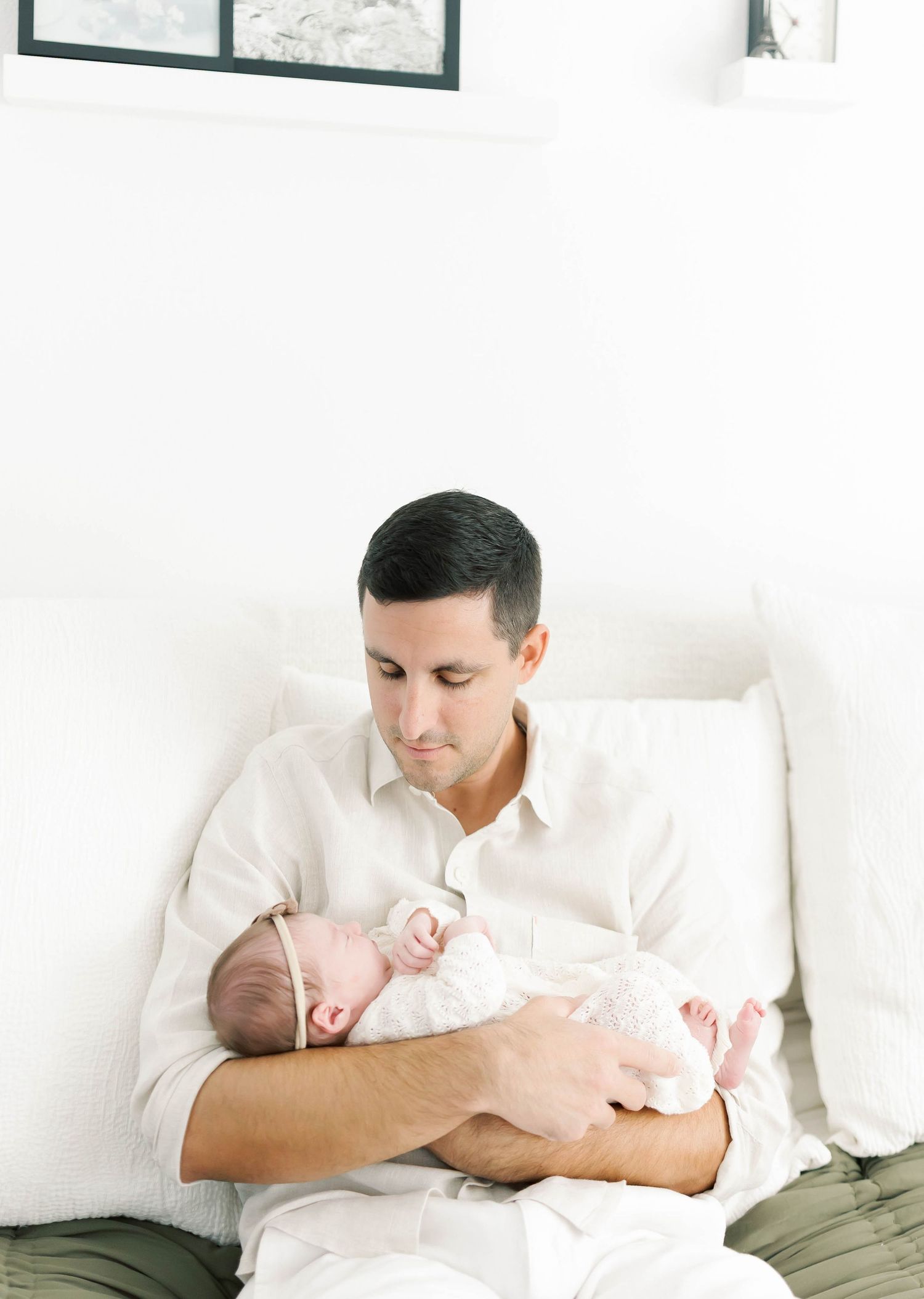 Intimate portrait of parent cradling sleeping newborn against white background.