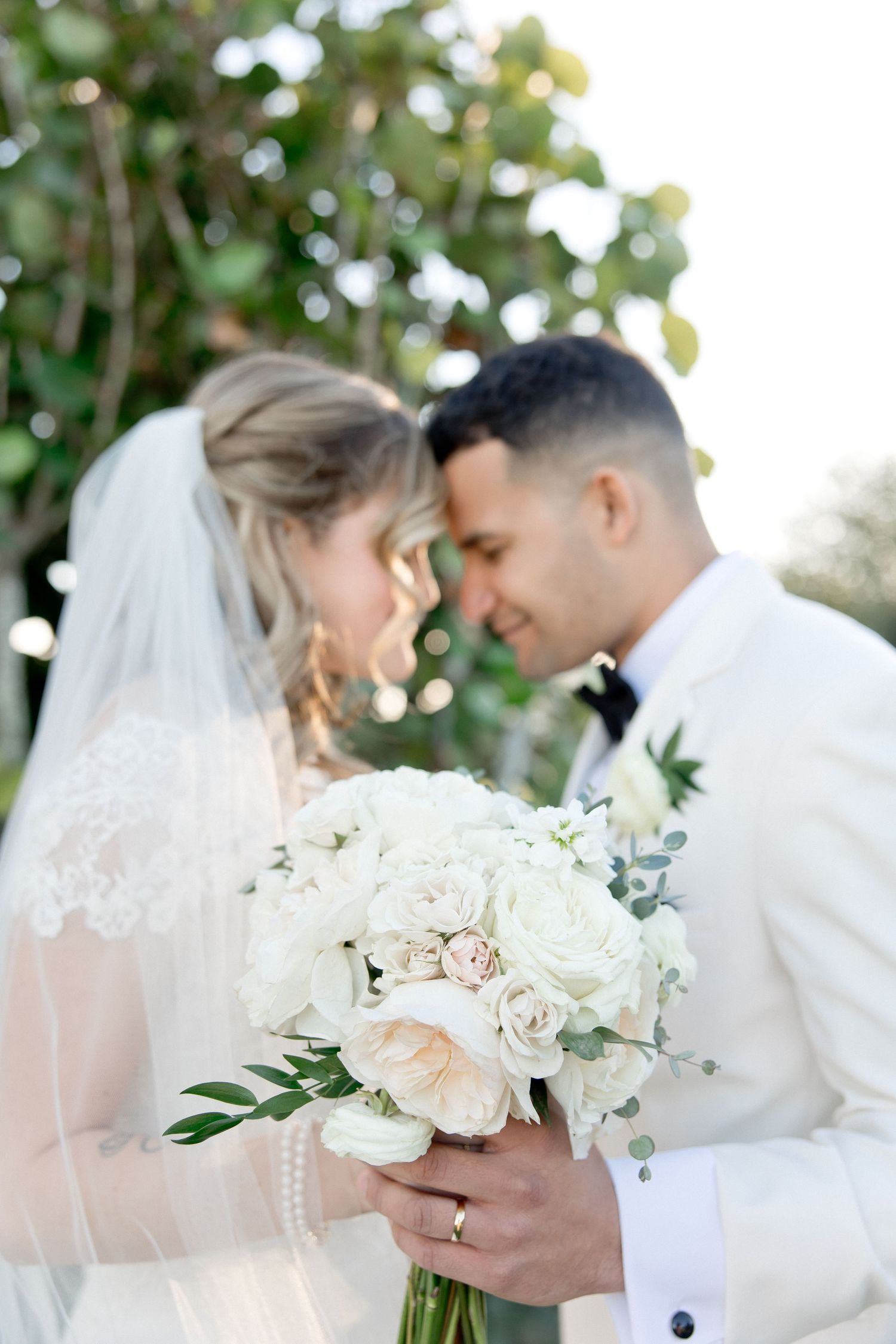 A delicate white and blush rose wedding bouquet held against formal wedding attire.