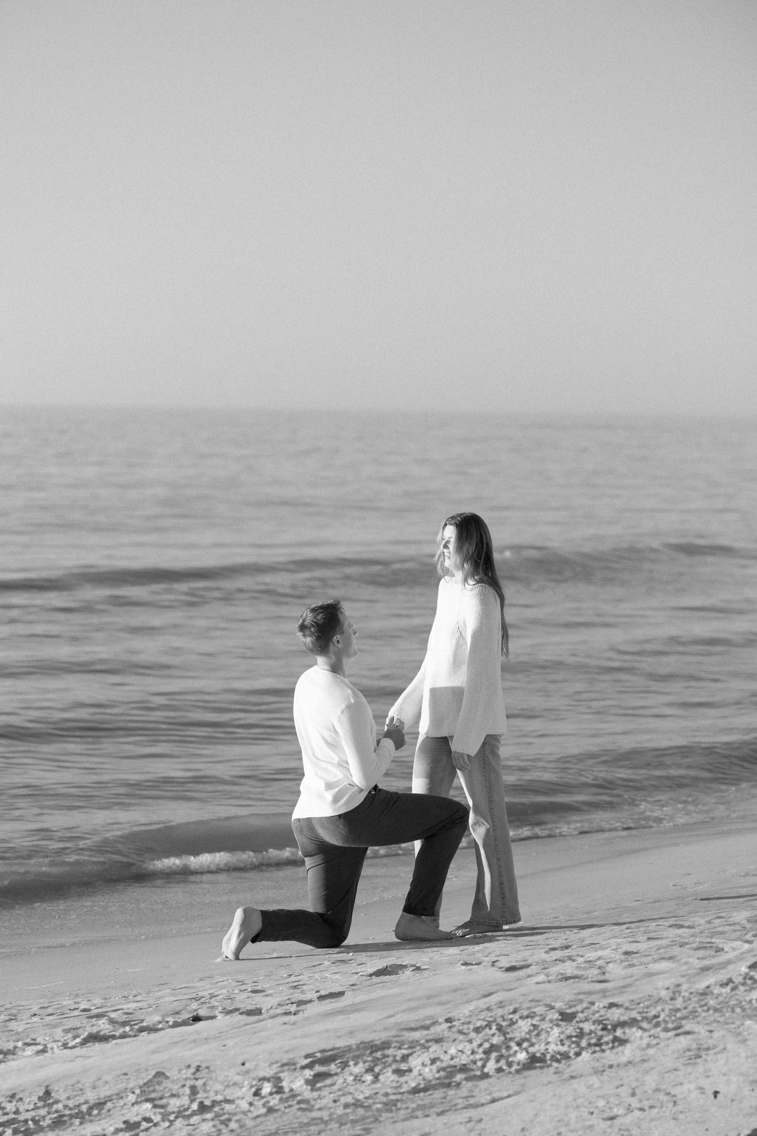 Black and white photo of couple sitting on beach chairs by the ocean.