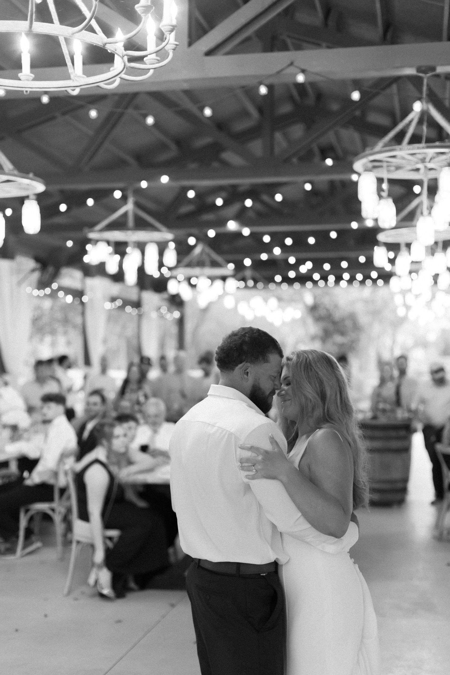 Black and white reception photo with string lights and chandeliers creating romantic ambiance.