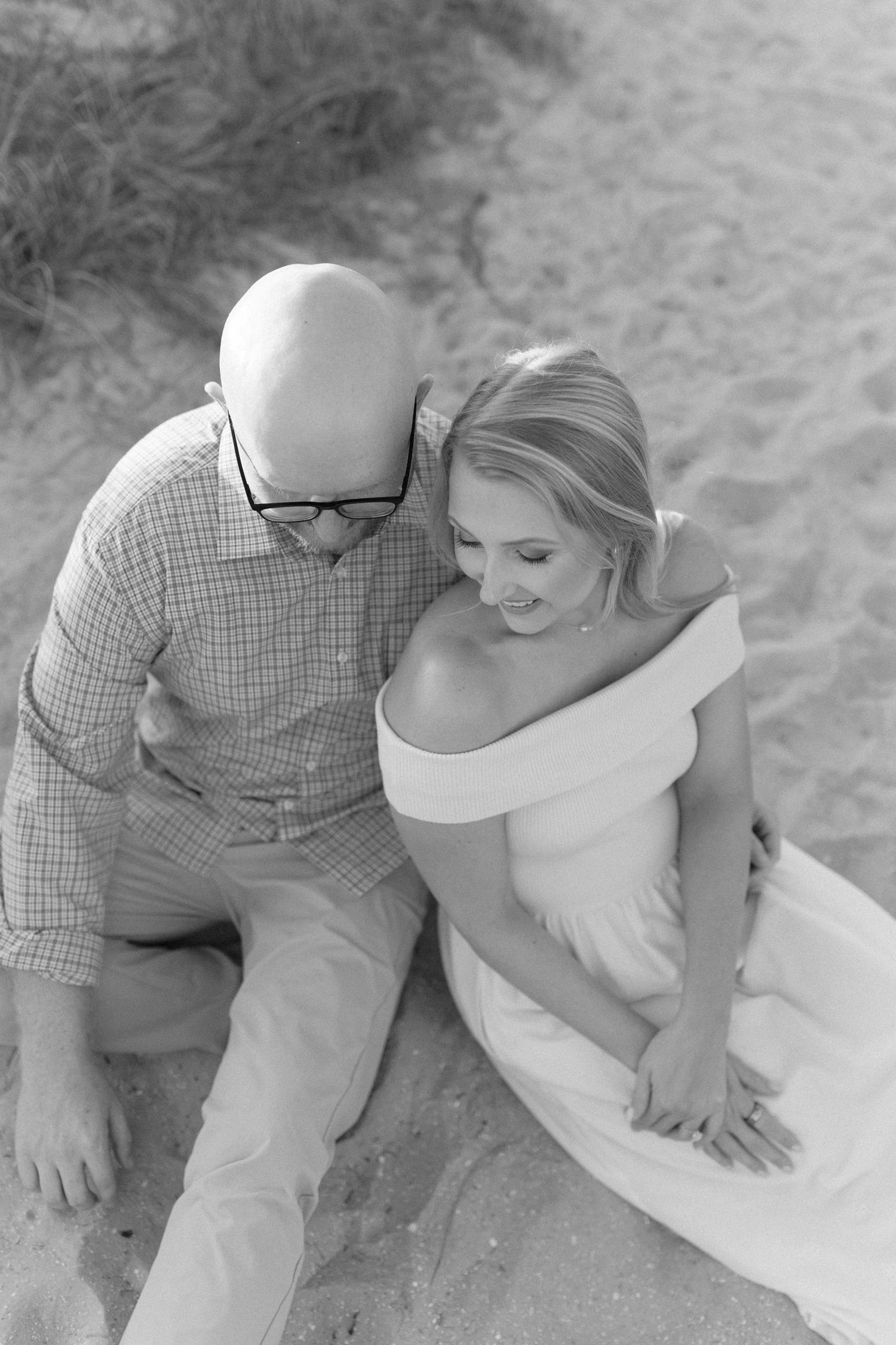 A romantic couple sitting close together on a sandy beach during a photo session.