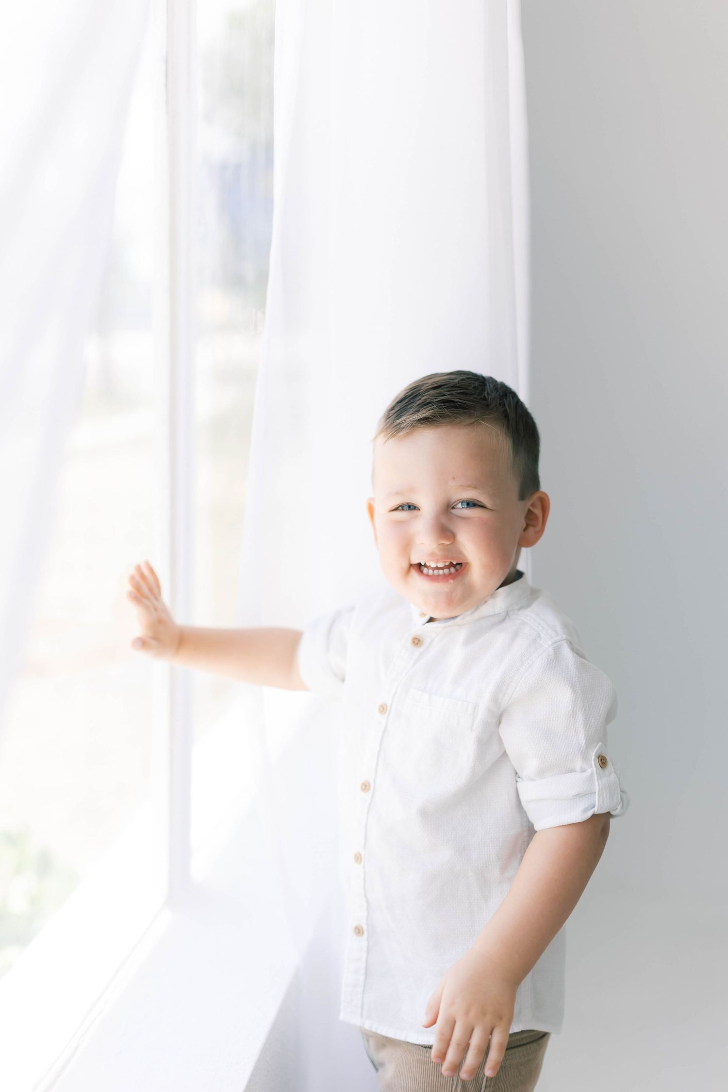 Bright and cheerful child portraits in white button-down shirt against light background.