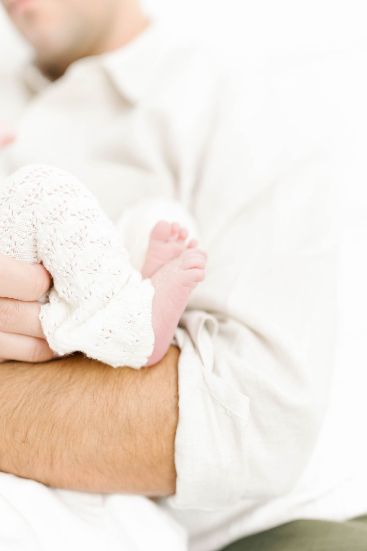 Intimate portrait of newborn baby being held in soft white clothing.