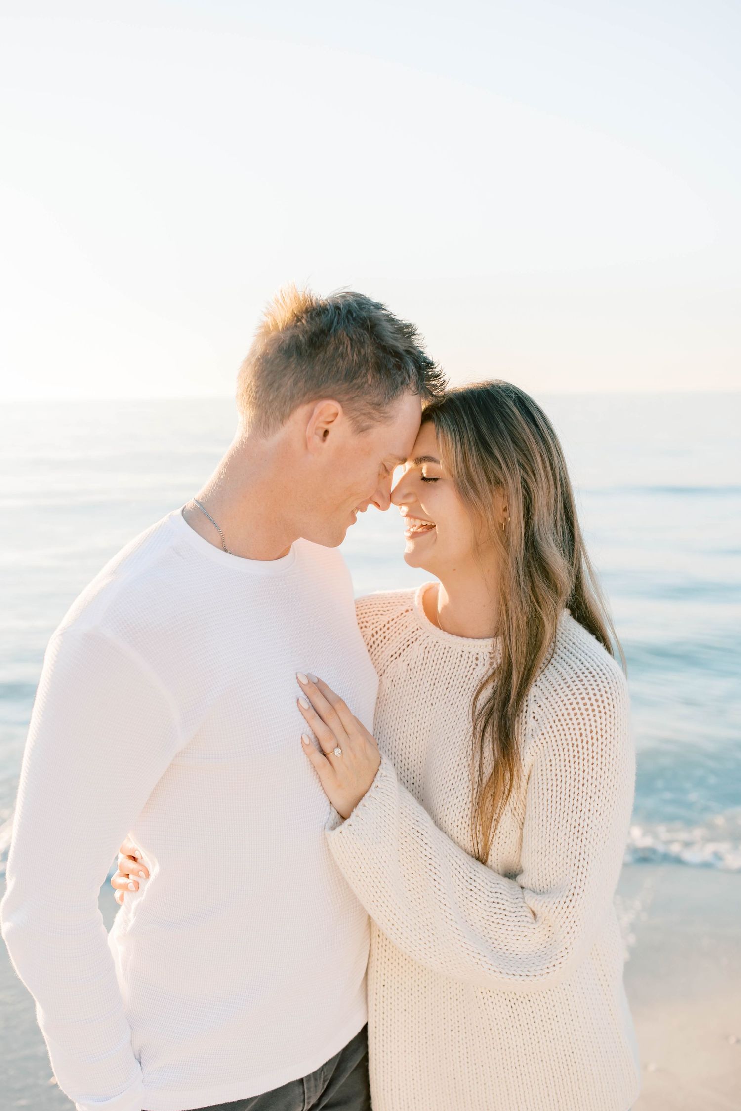 A romantic moment between a couple in matching white sweaters on a beach.