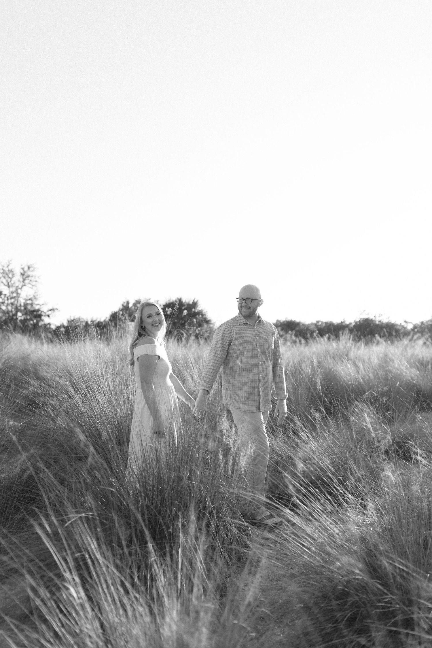 Black and white image of a couple standing together in a field of wild grass.