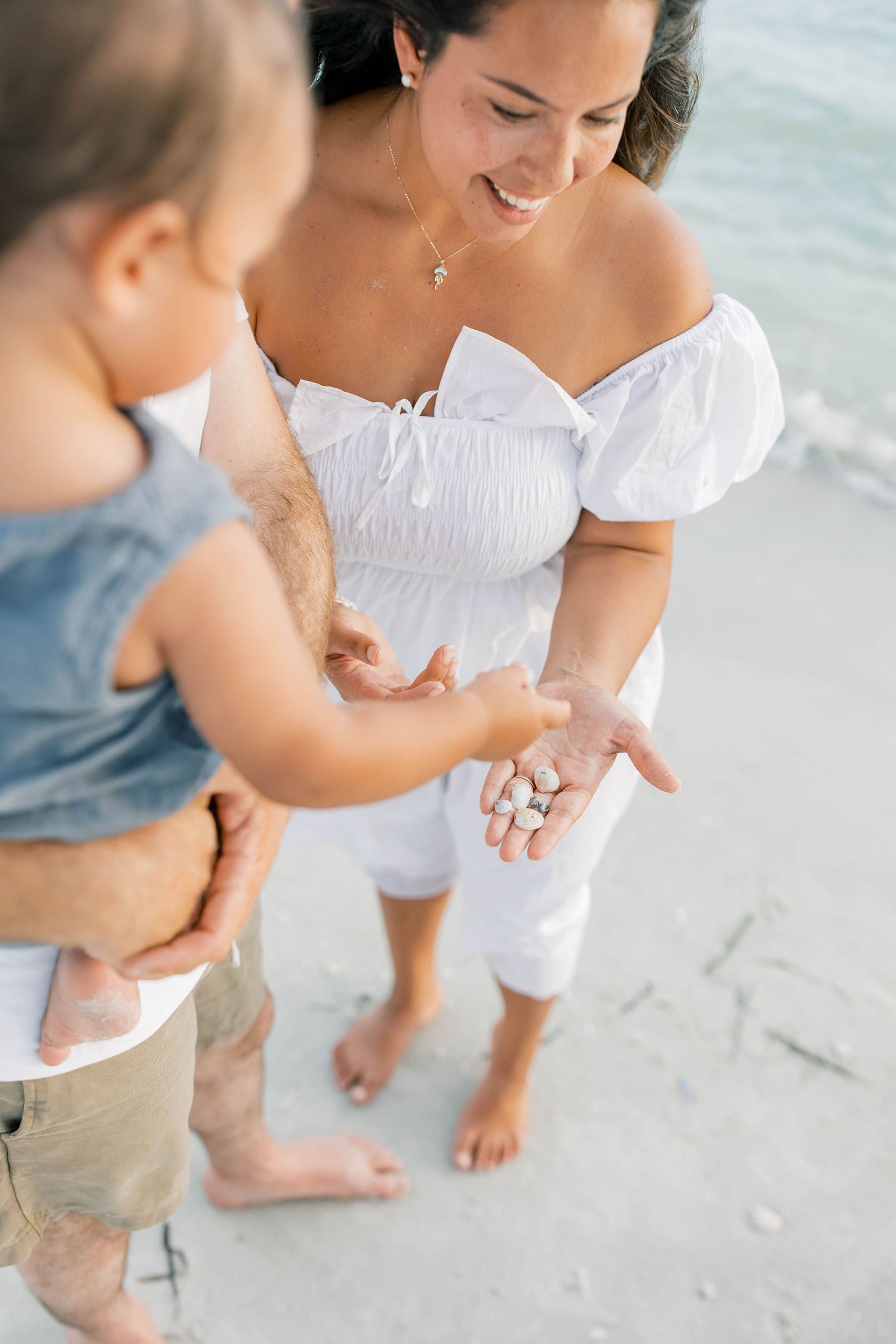 Close-up view of family members' feet and legs as they stand together on a sandy beach.
