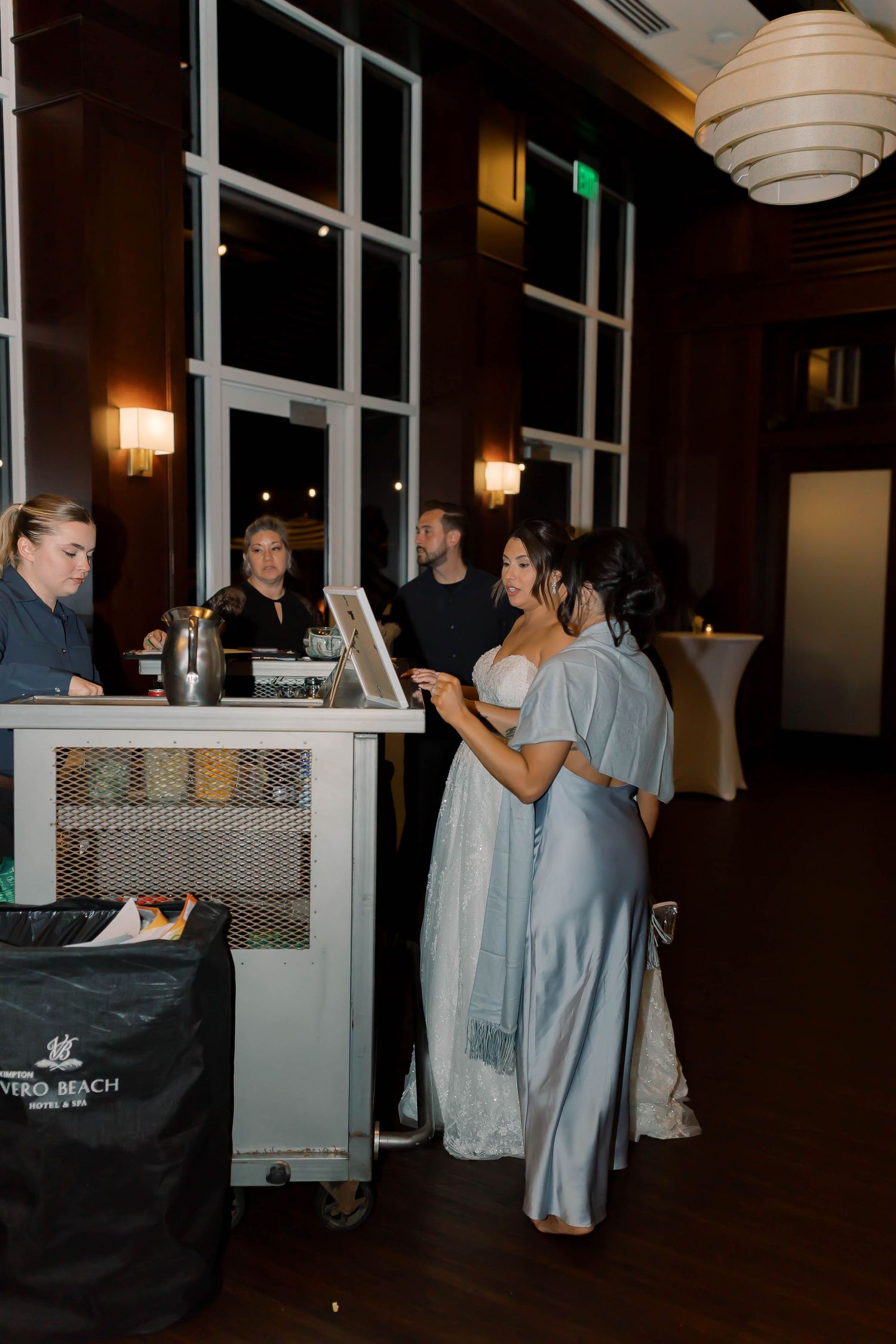 Bride in light blue reception dress uses photo booth with guests in warmly lit venue.