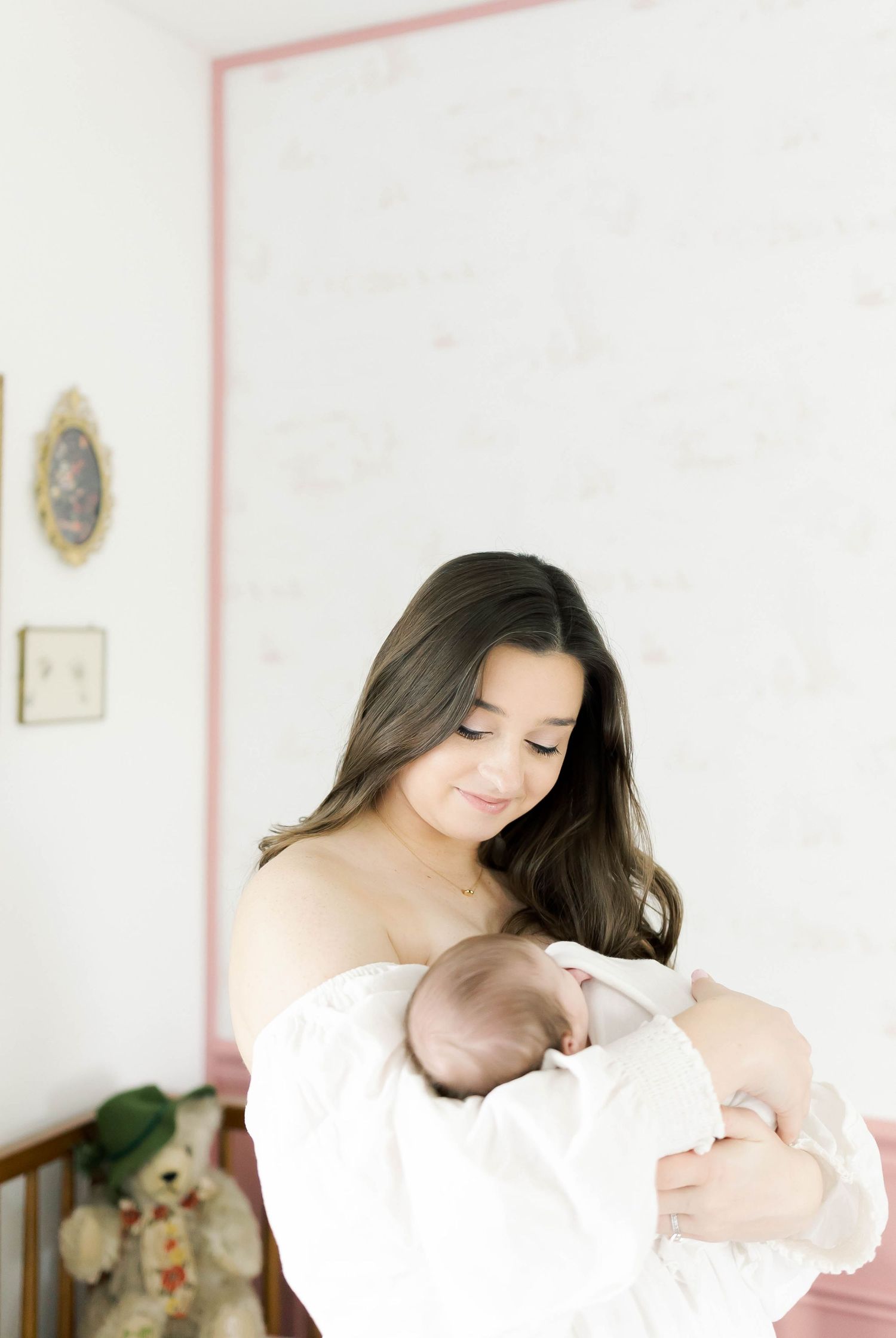 Tender moment between parent and baby in white nursery with pink walls.