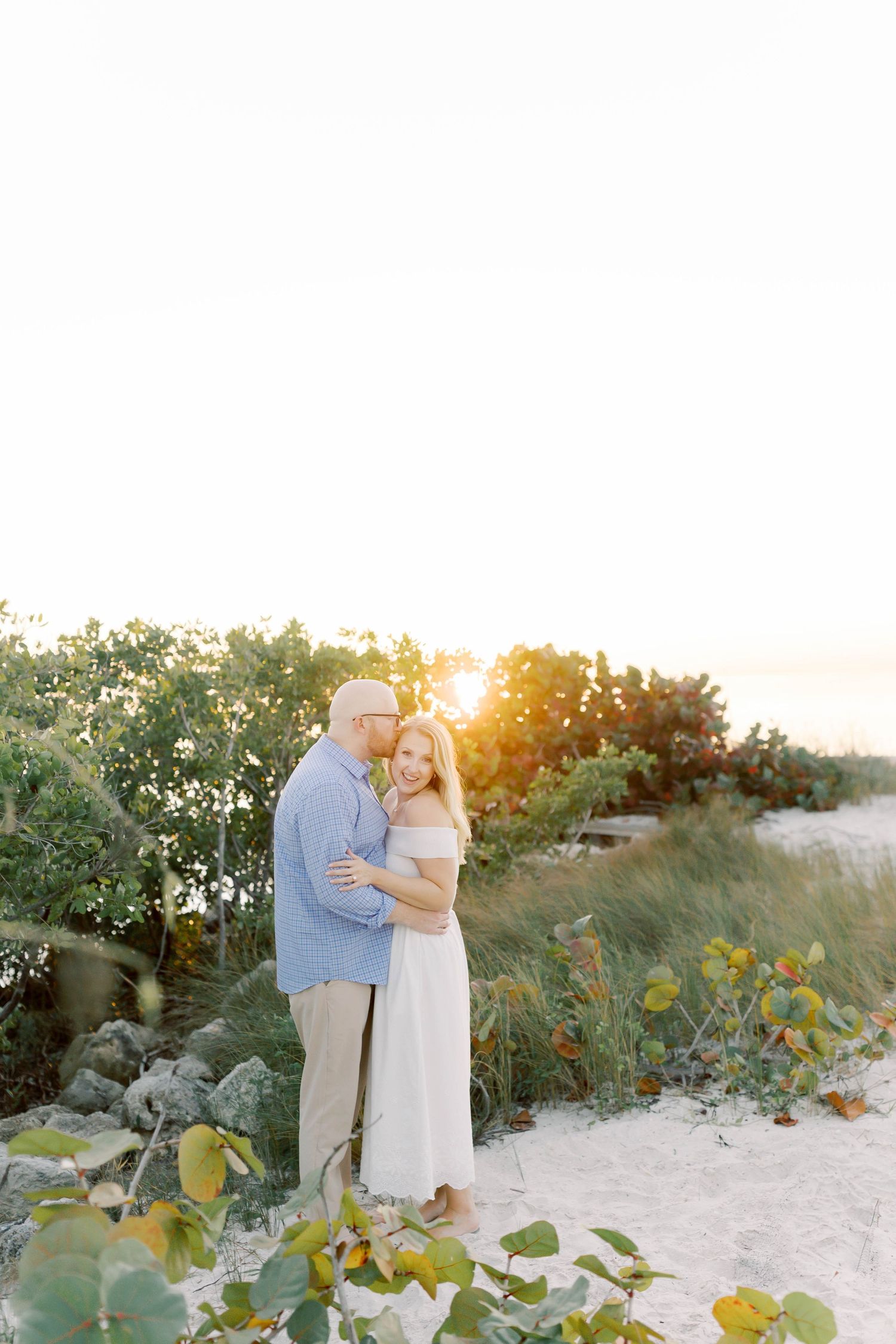 Romantic beach portraits with couple walking through seaside greenery at sunset.