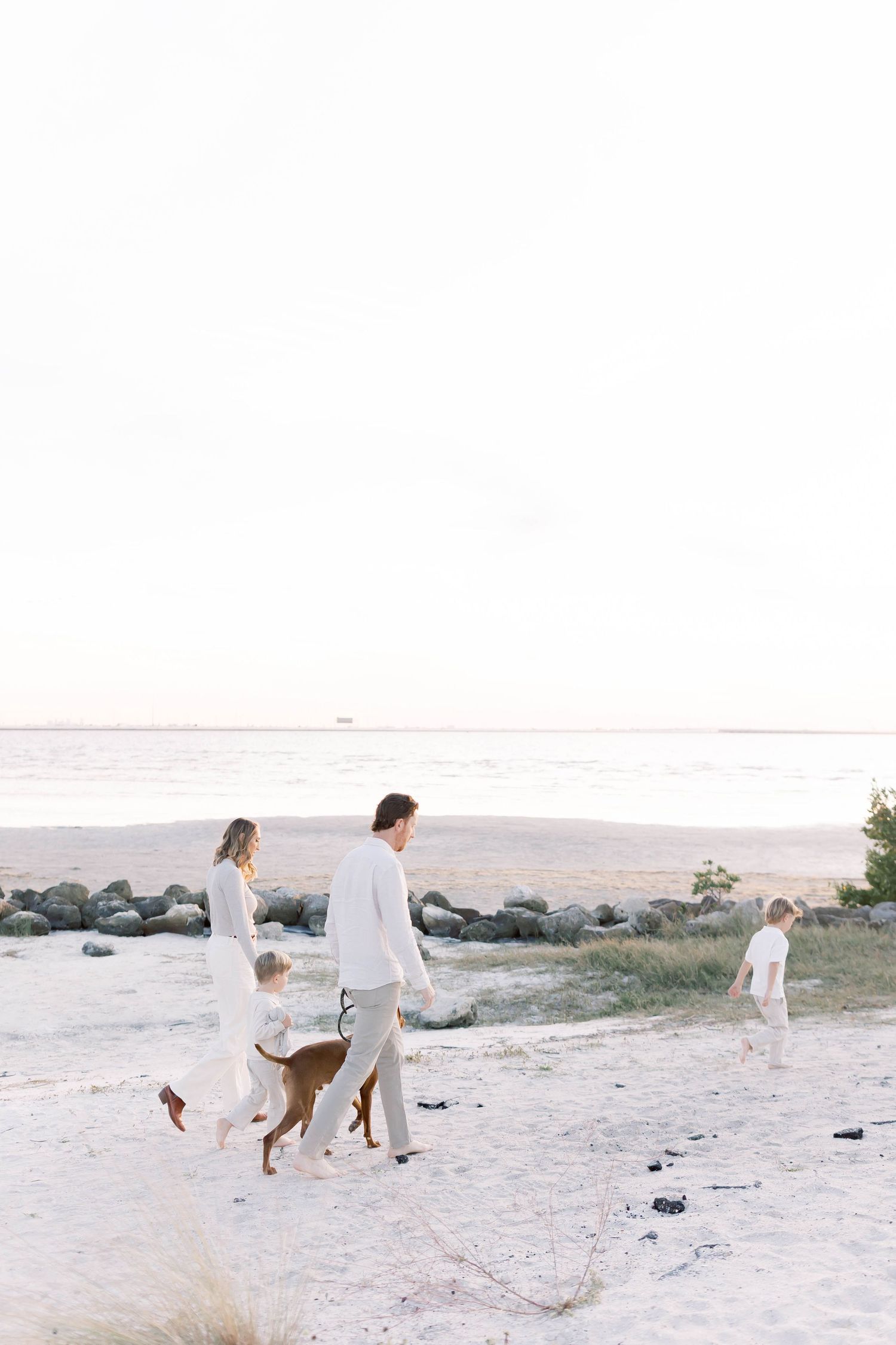 Family walking together on beach with rocks and ocean in background during sunset.