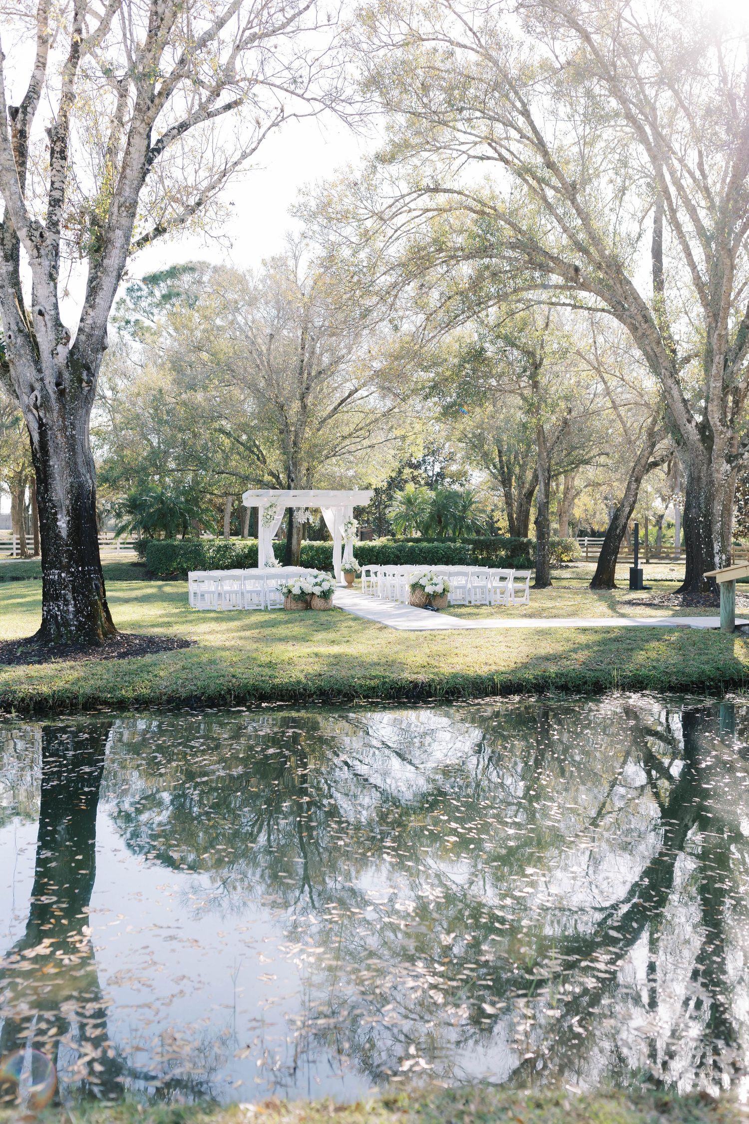 Panoramic view of a lakeside wedding venue with white chairs and decorative pergola.