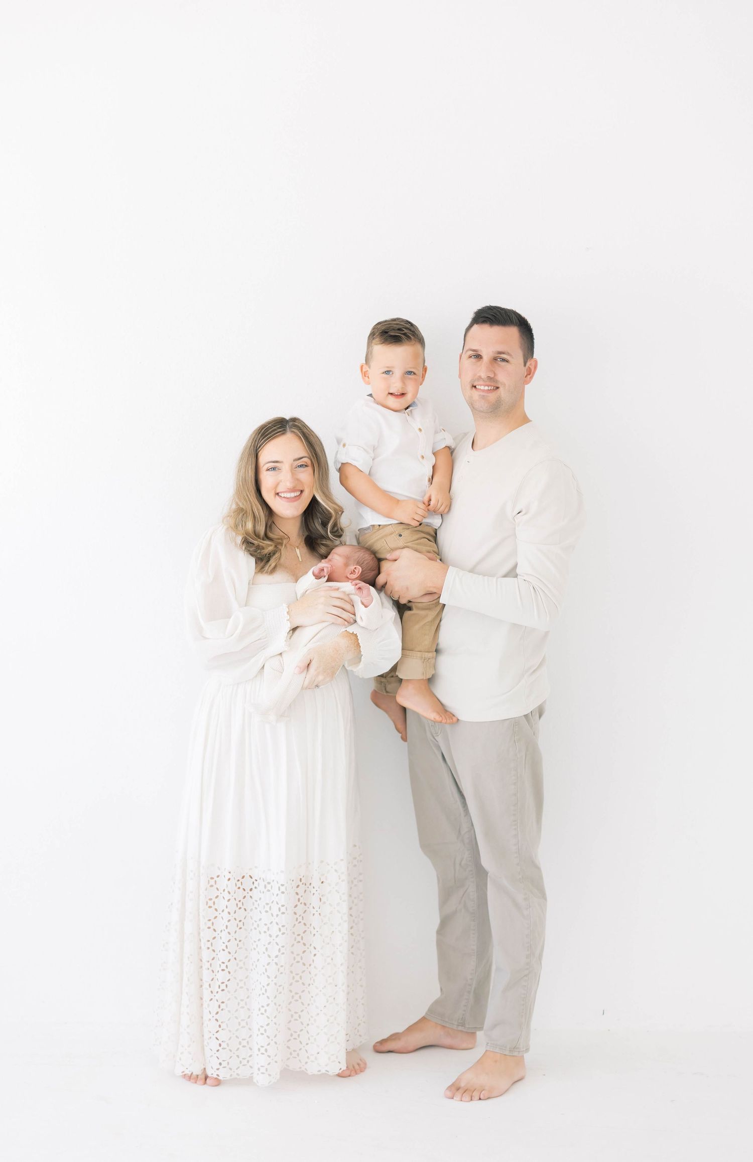 Minimalist family photo with parents and children wearing white against bright background.