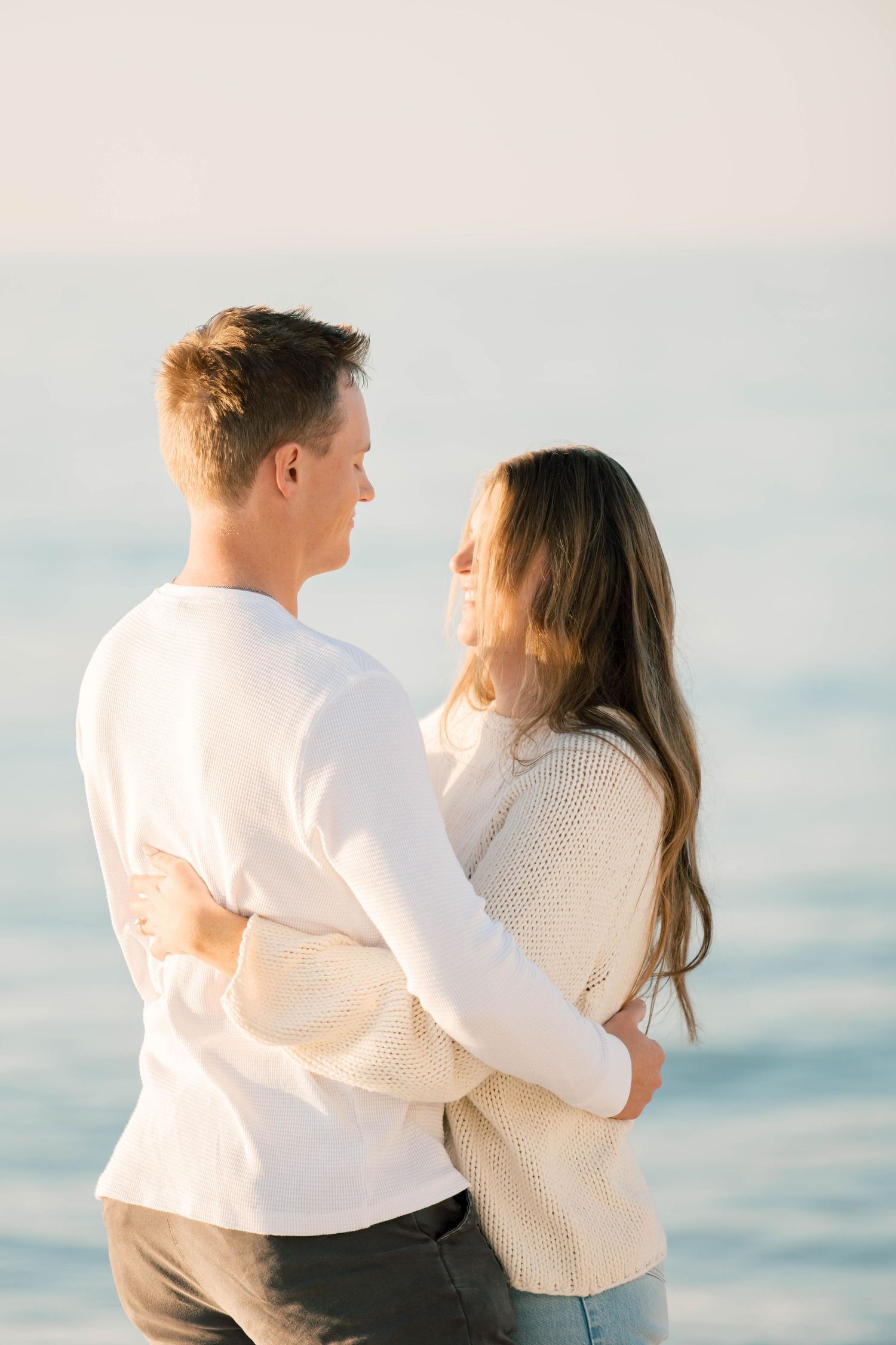 Two people in white sweaters share an intimate moment against a serene ocean backdrop.