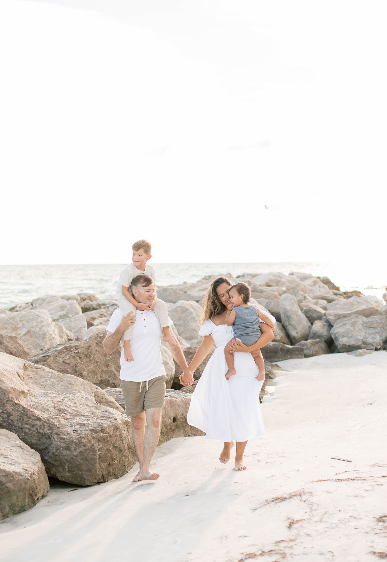 Family walking and playing together along a bright sandy shoreline.