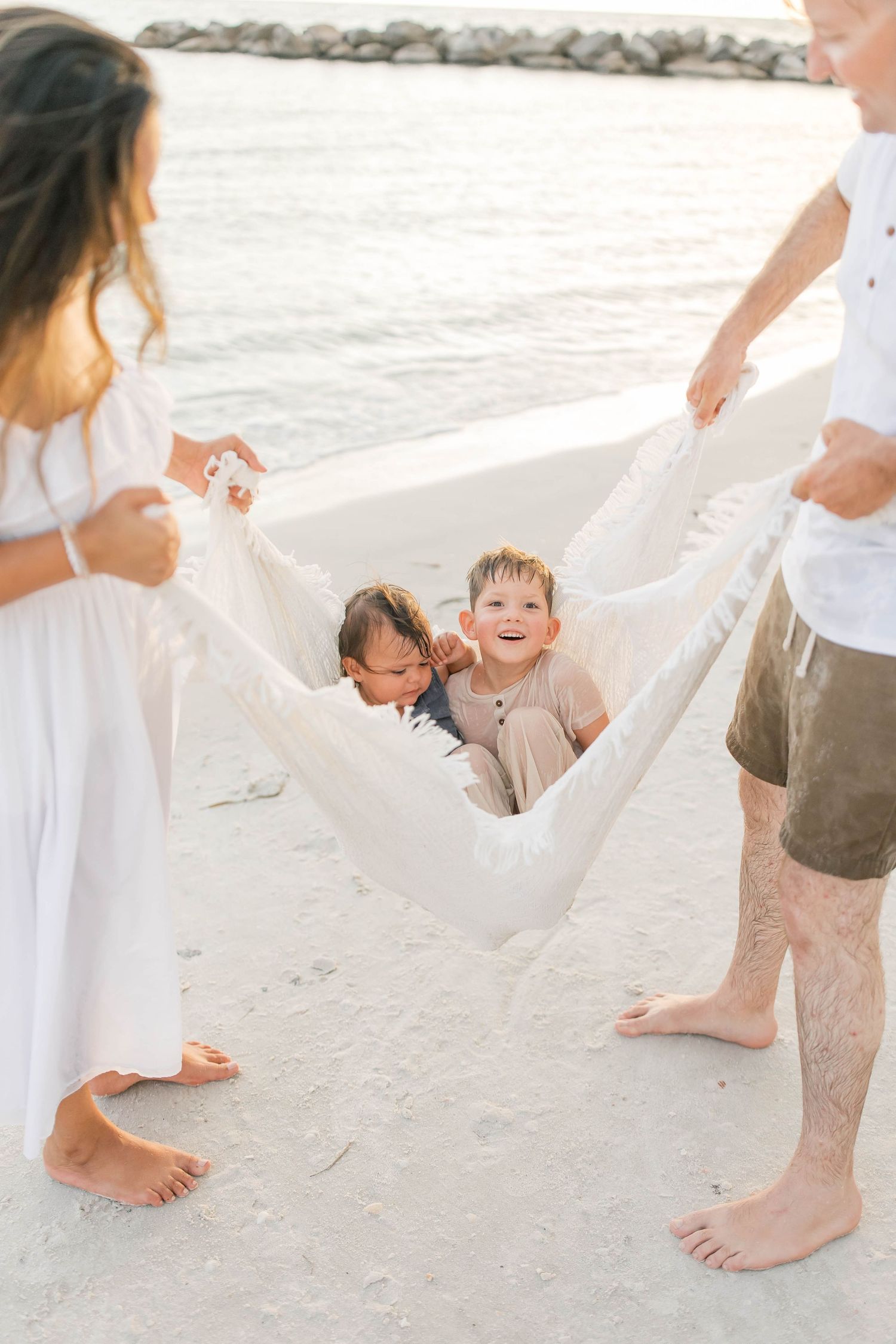 Joyful family interactions on a sandy beach with white fabric flowing in the breeze.