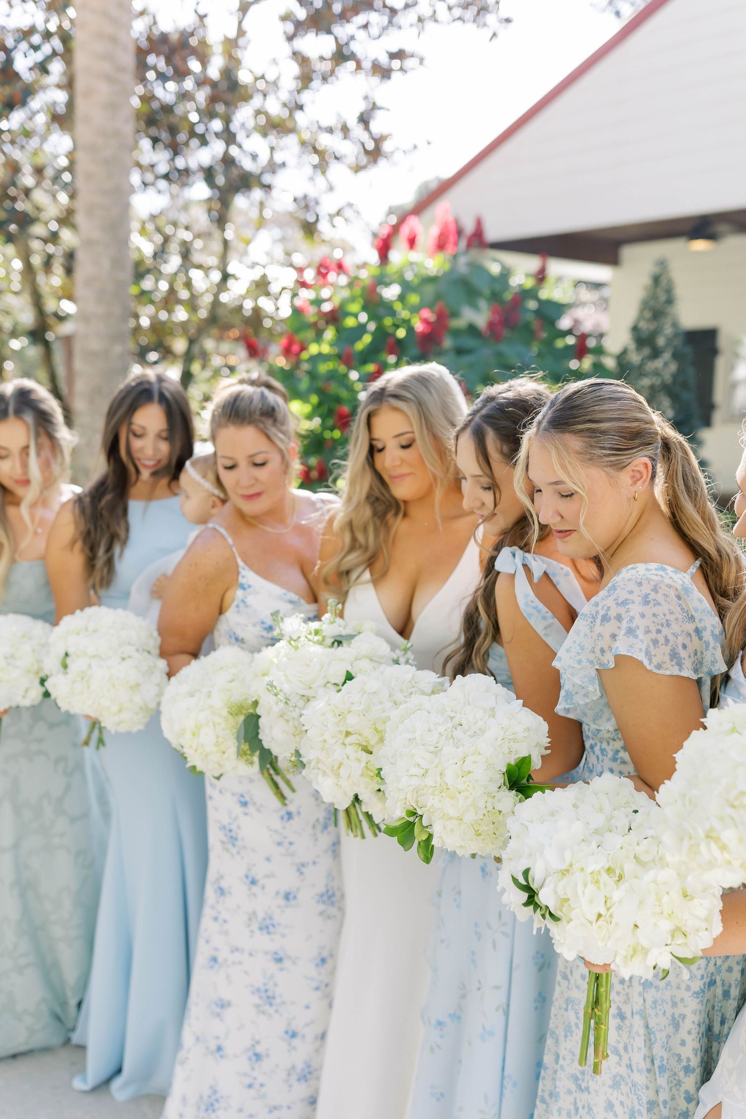 Bridesmaids in pastel blue dresses hold white bouquets while laughing together.