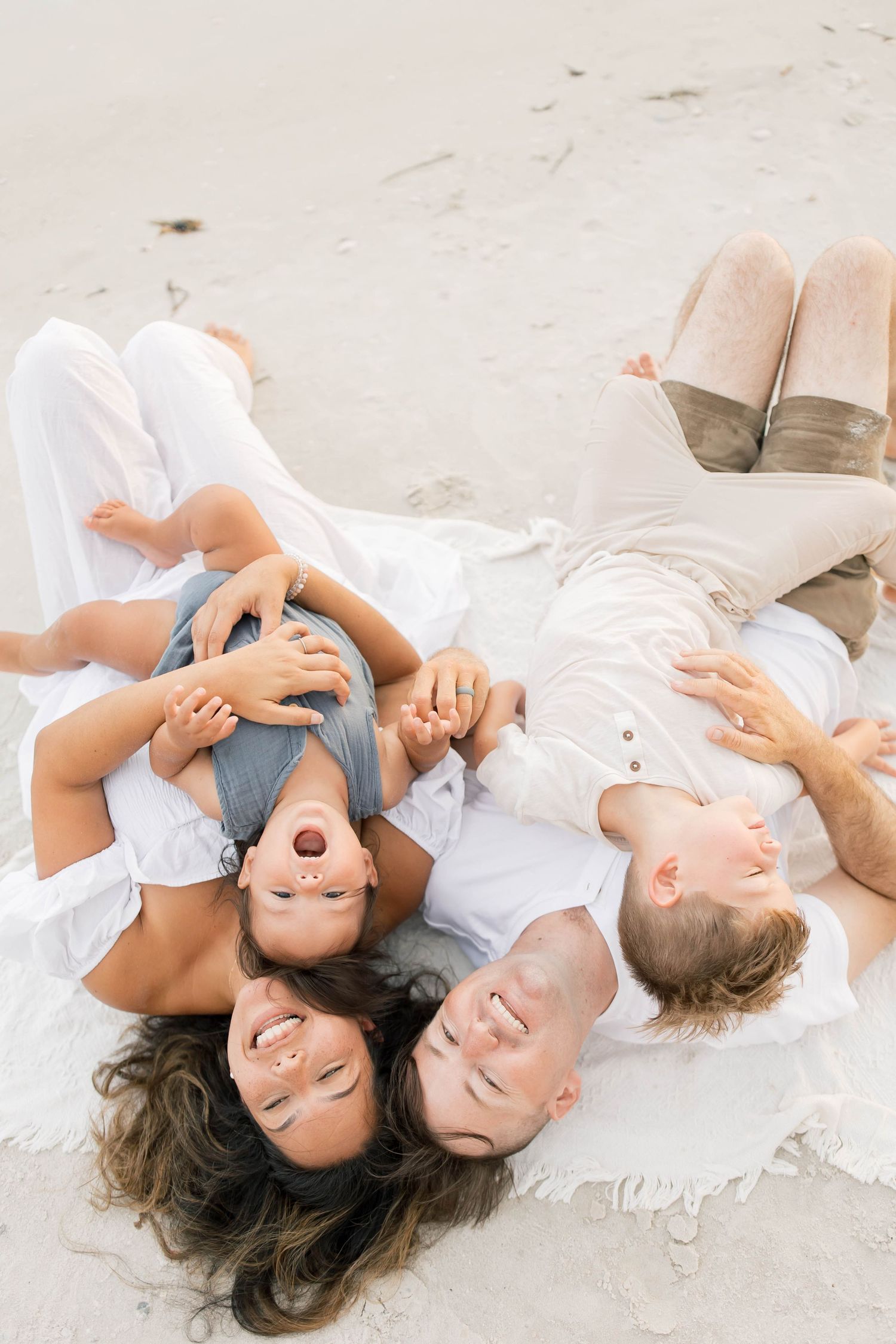 Intimate family moments captured while relaxing on white beach blanket.