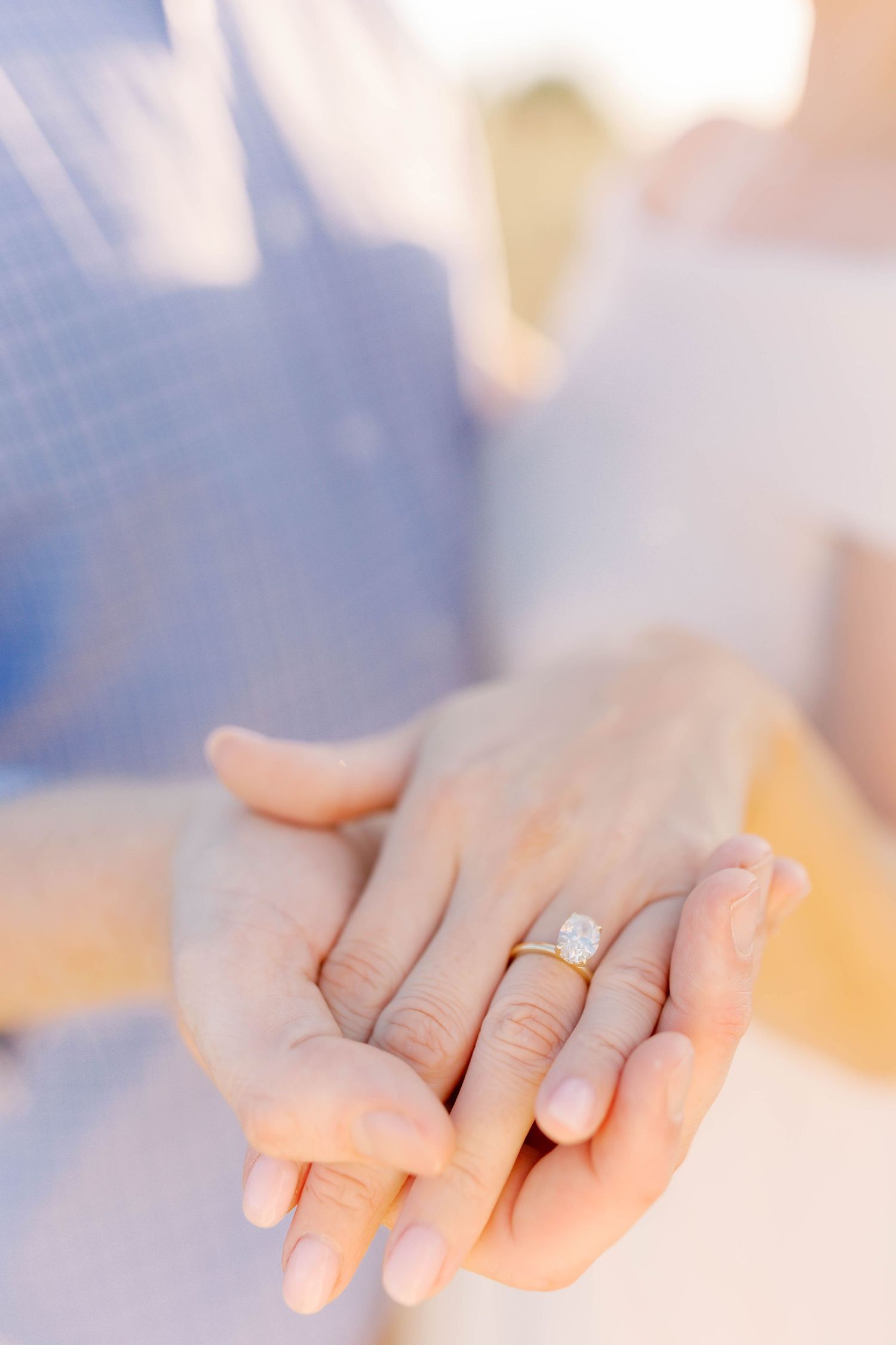 Close-up of hands with engagement ring in soft, dreamy lighting.